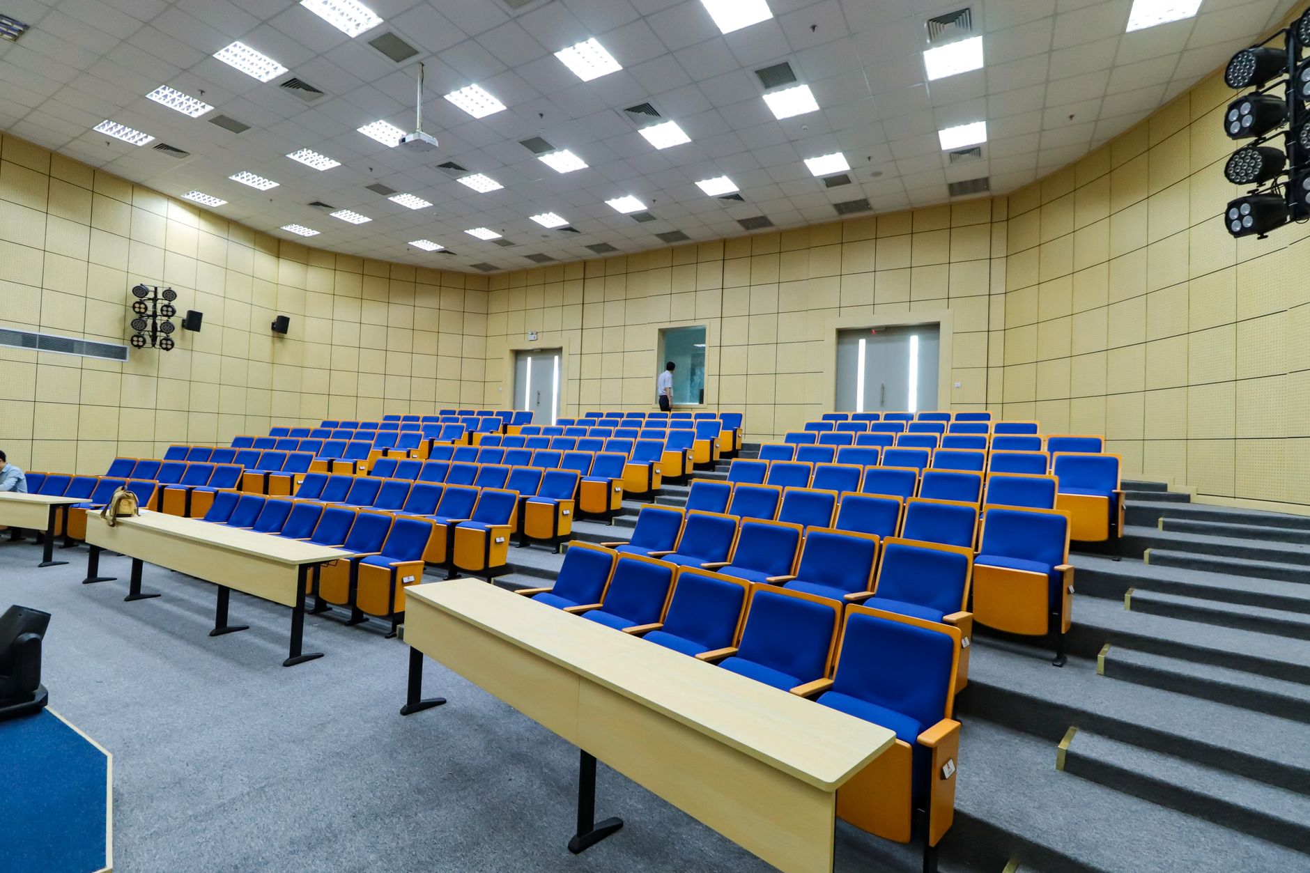 a congressional hearing room viewed from the back, rows of empty chairs facing a raised dais, institutional lighting overhead