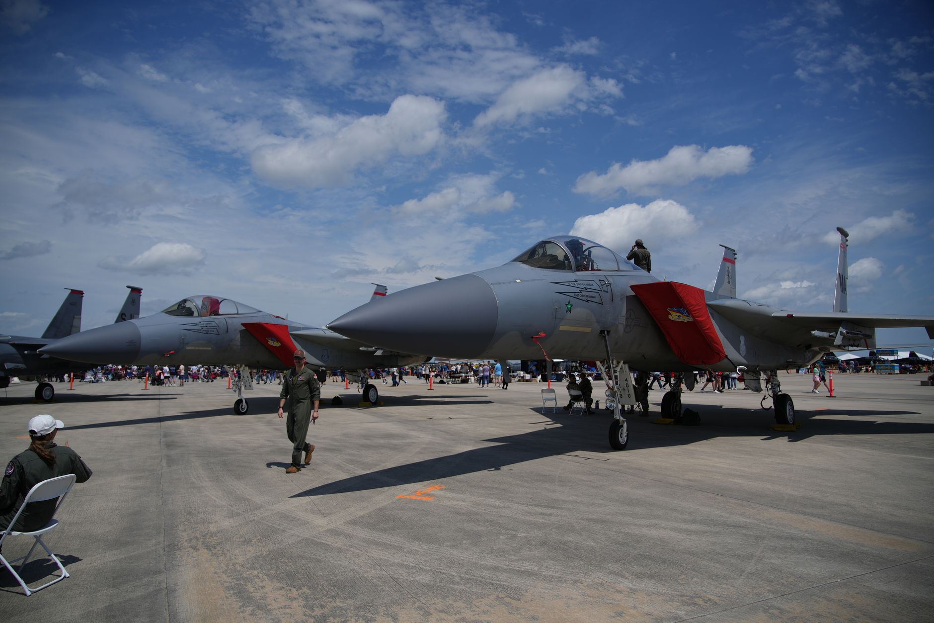 an F-15E Strike Eagle parked on a flight line at a U.S. Air Force base, concrete ramp visible in the background with maintenance equipment nearby