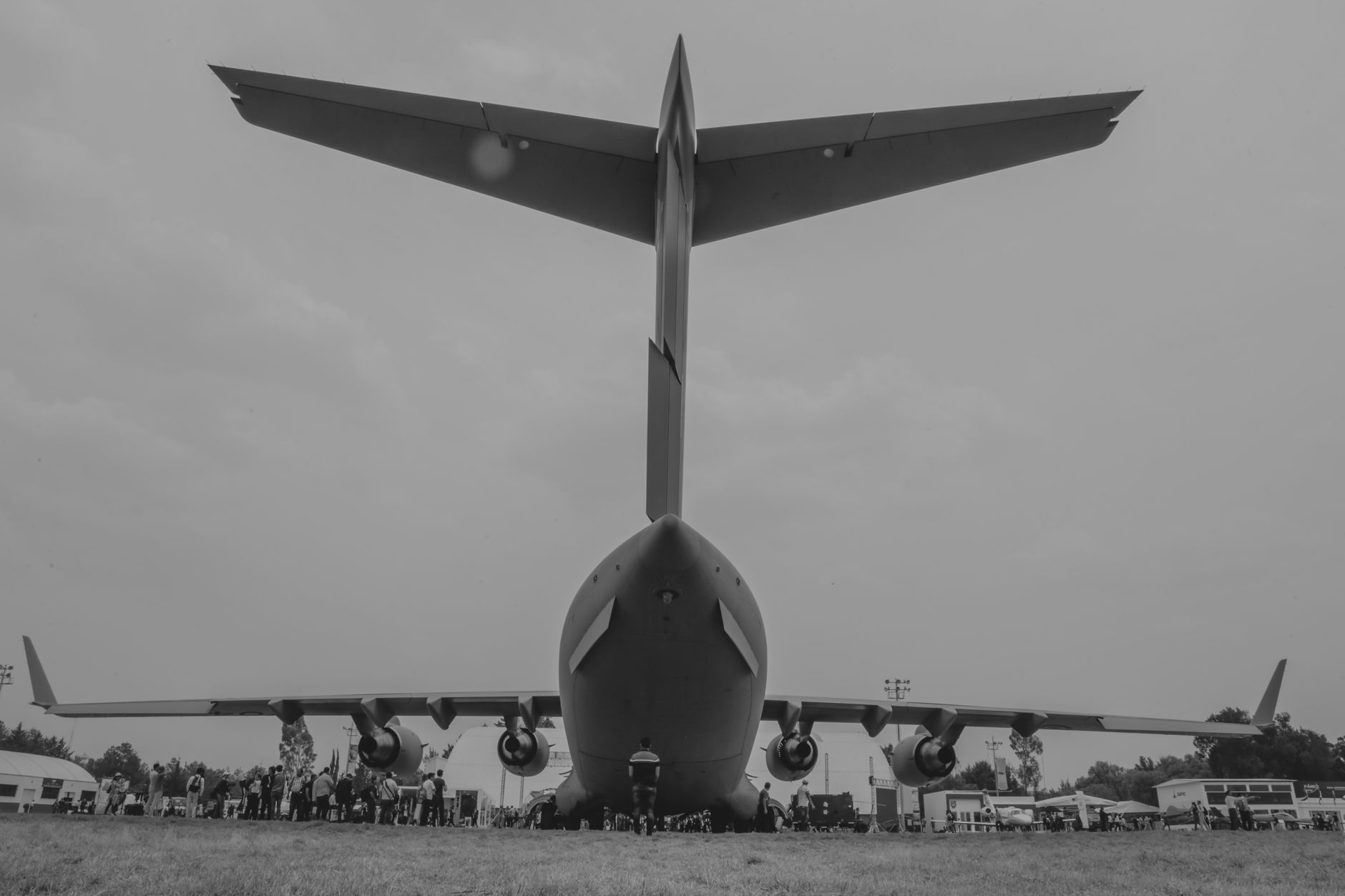 wide-angle view of a large airshow exhibition hall with missile defense system mockups and electric aircraft displayed side by side, visitors moving between exhibits in the background