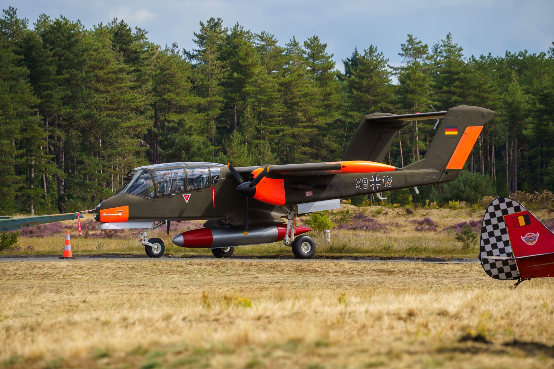 a sleek electric vertical takeoff and landing aircraft prototype parked on an outdoor airshow static display apron, tarmac and hangars visible in the background