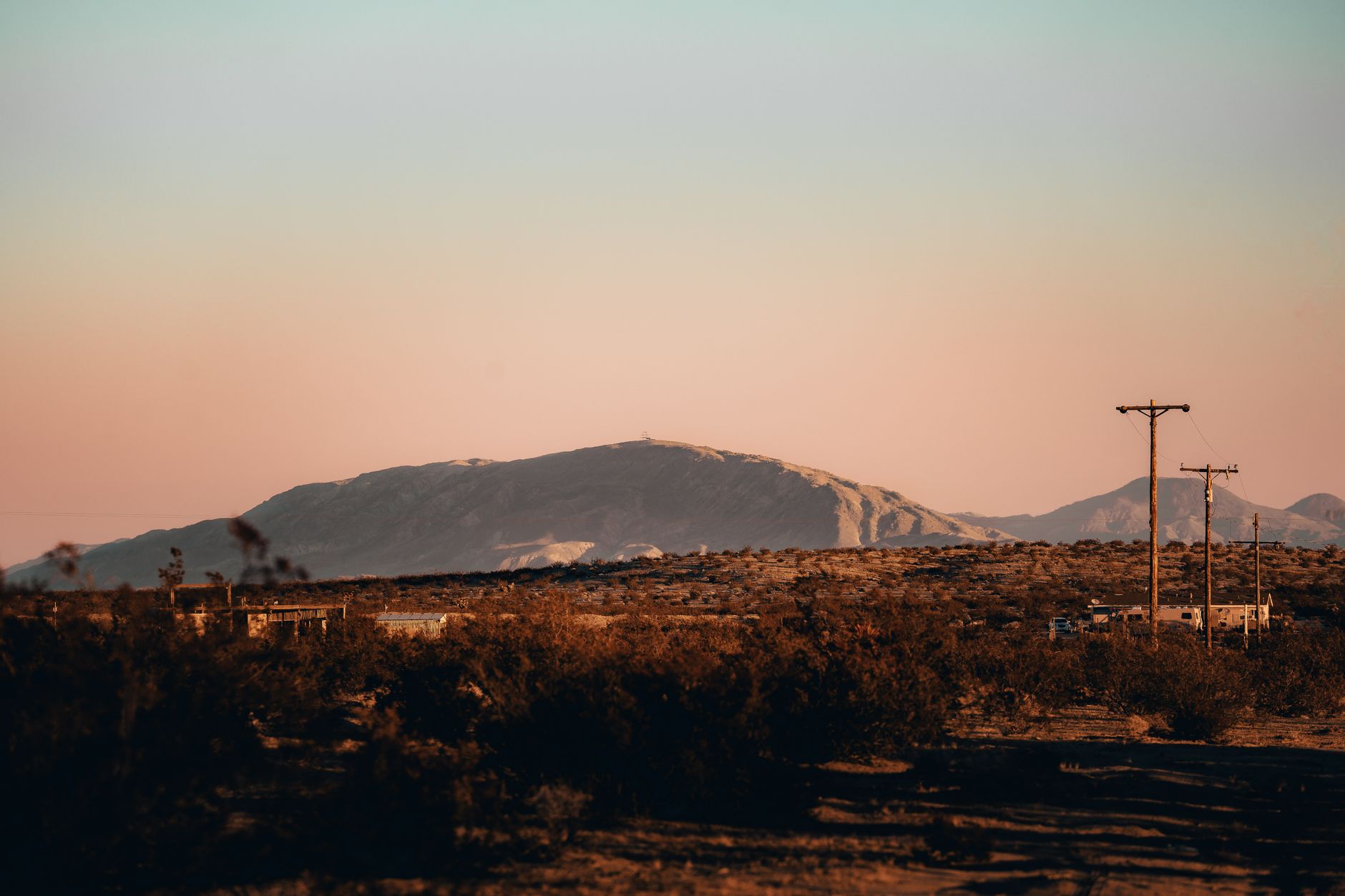 wide shot of a desert military installation at Fort Bliss with rows of temporary and semi-permanent housing structures visible against a flat terrain backdrop, mountains in the distance