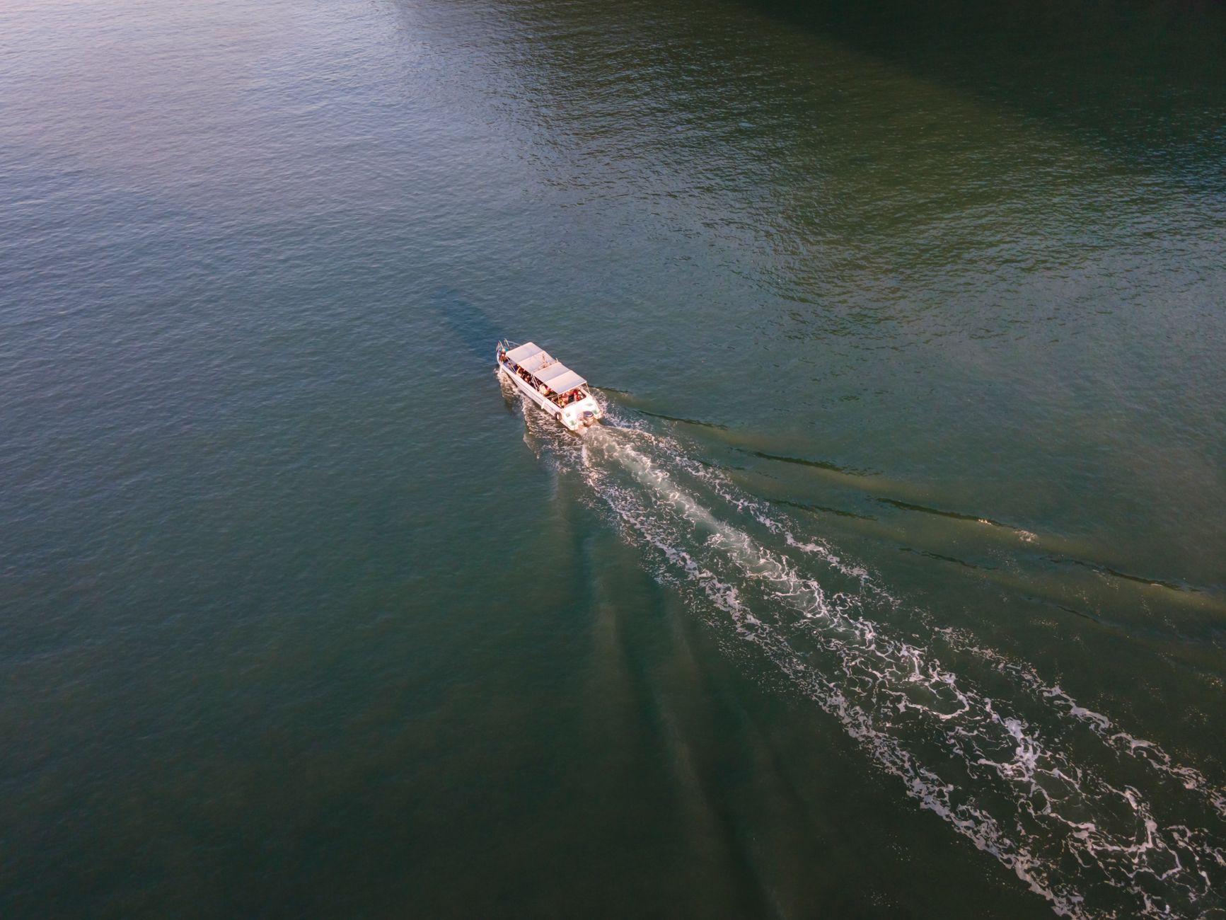 a small high-speed autonomous surface vessel moving at speed across open ocean, wake visible behind a low-profile hull, no crew visible on deck