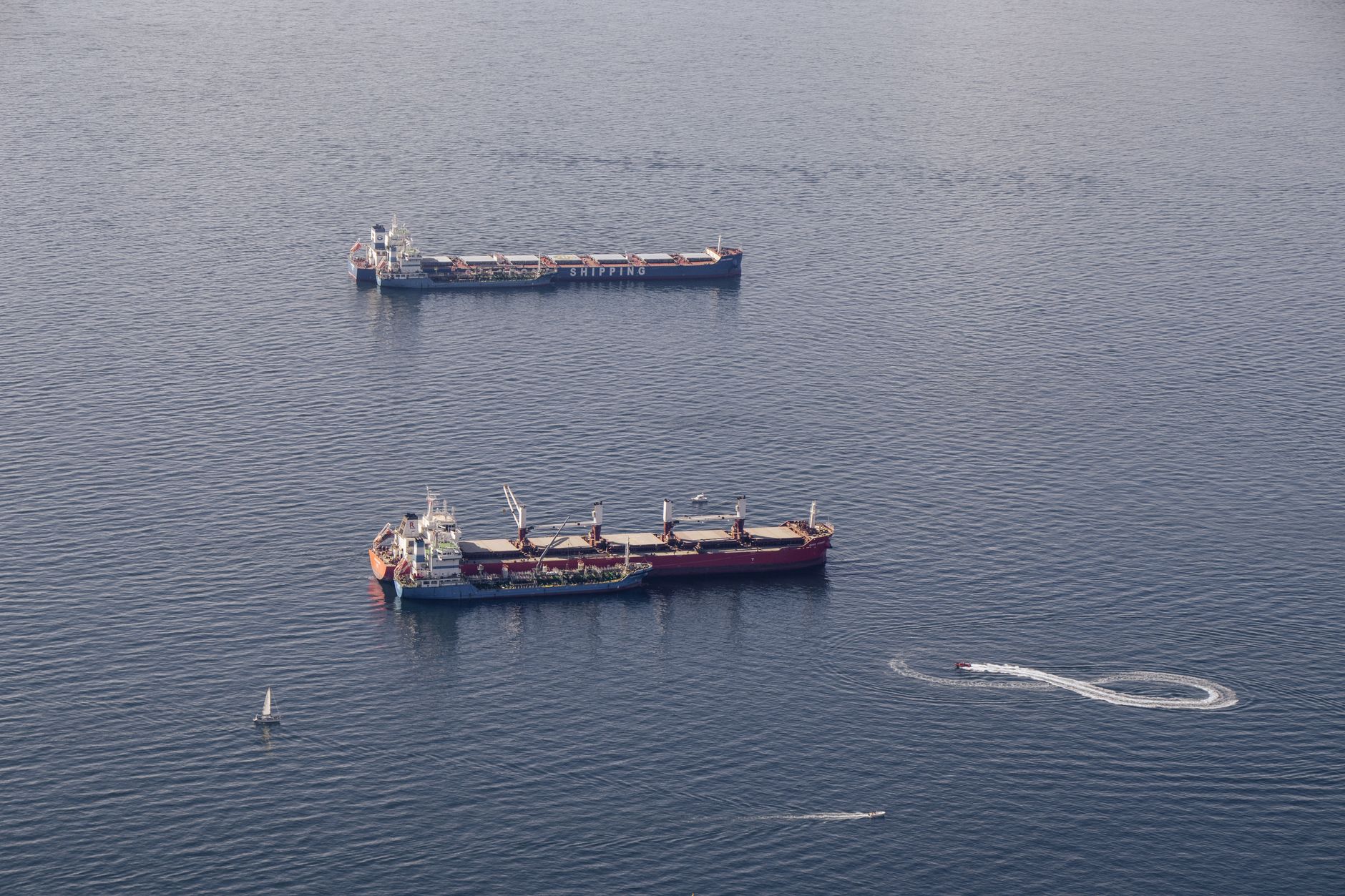 a large crude oil tanker transiting a narrow maritime chokepoint, viewed from an elevated coastal vantage point, calm blue water surrounding the vessel