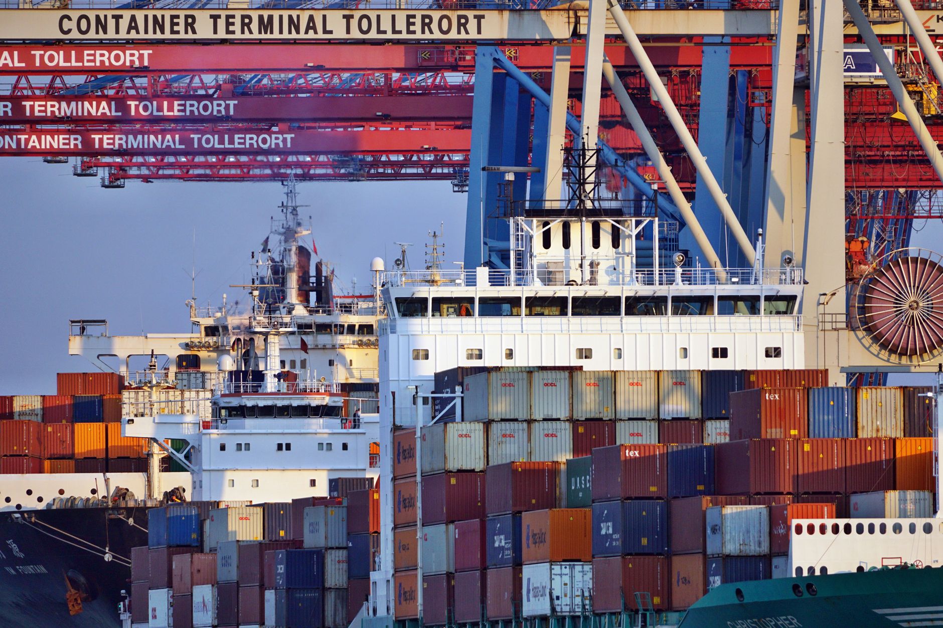 a wide aerial view of a major port and commercial shipping terminal with container vessels docked, no people in foreground