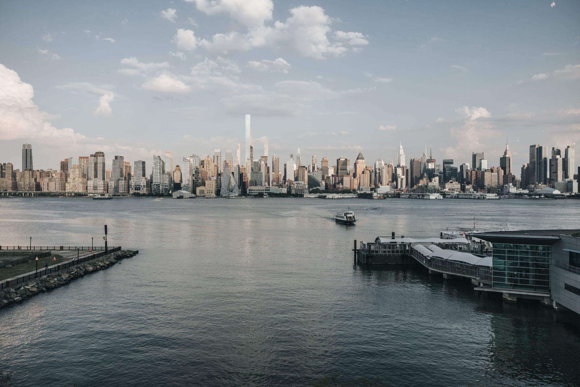 a wide shot of Manhattan's midtown skyline viewed from across the East River, commercial towers reflected in the water at dusk, no people visible in the foreground