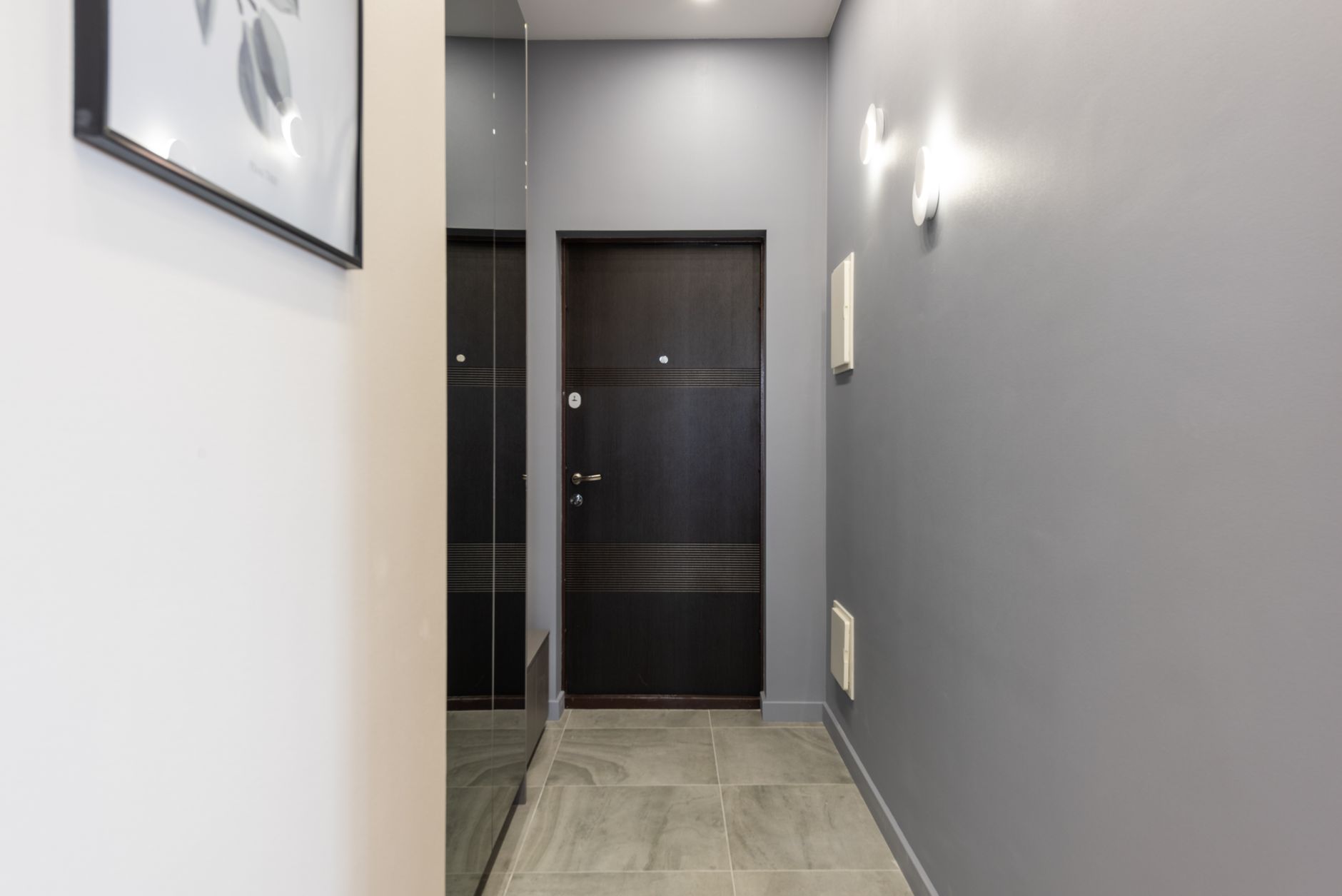 interior corridor of a furnished temporary residential facility showing numbered unit doors, overhead lighting, and clean tiled floors in an institutional but modern setting