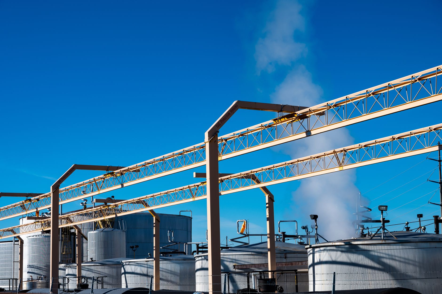 rows of large above-ground oil storage tanks at a coastal petroleum terminal, industrial infrastructure visible at dusk with crane outlines in the background