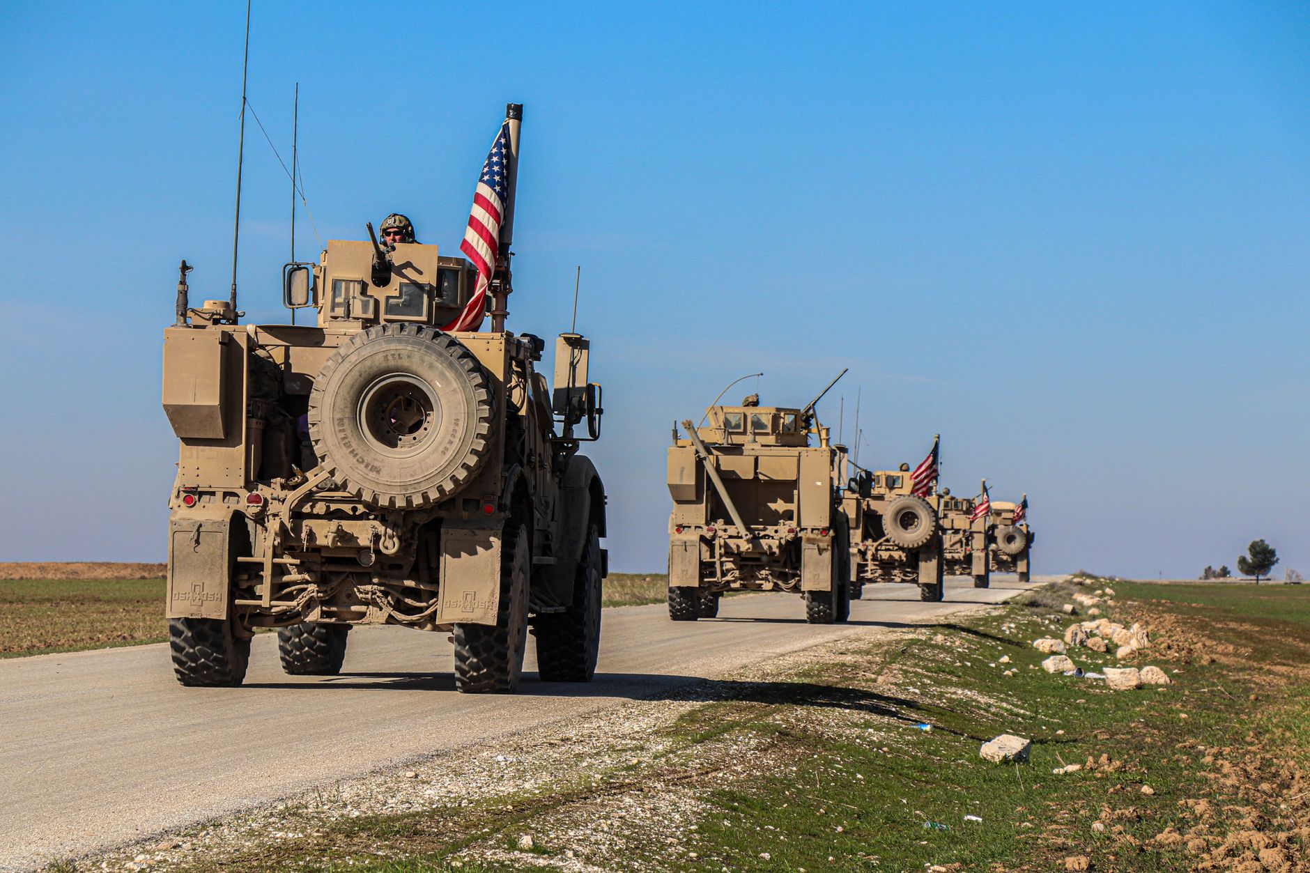 a Patriot air defense battery positioned in an open field, launcher units elevated against a clear sky, support vehicles visible nearby