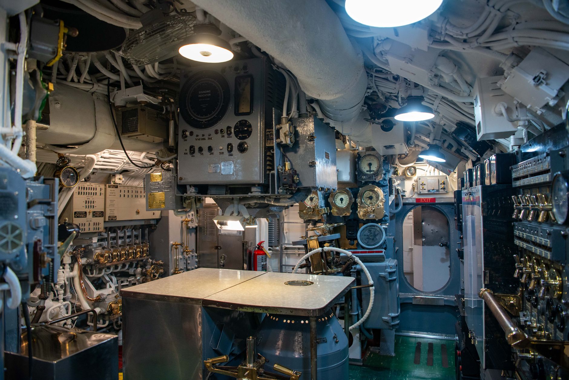 a large submarine pressure hull section under construction inside a covered naval shipyard drydock, with industrial lighting illuminating the curved steel framework