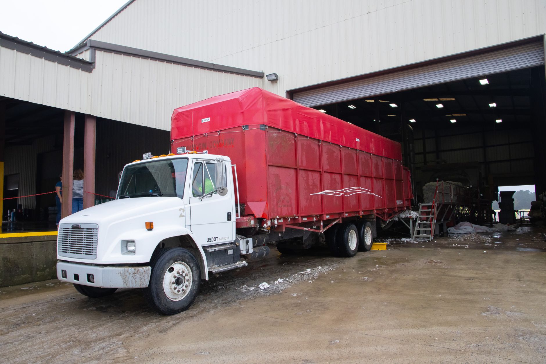 a row of commercial semi-trucks parked at a large logistics depot, with loading docks and warehouse facilities visible in the background