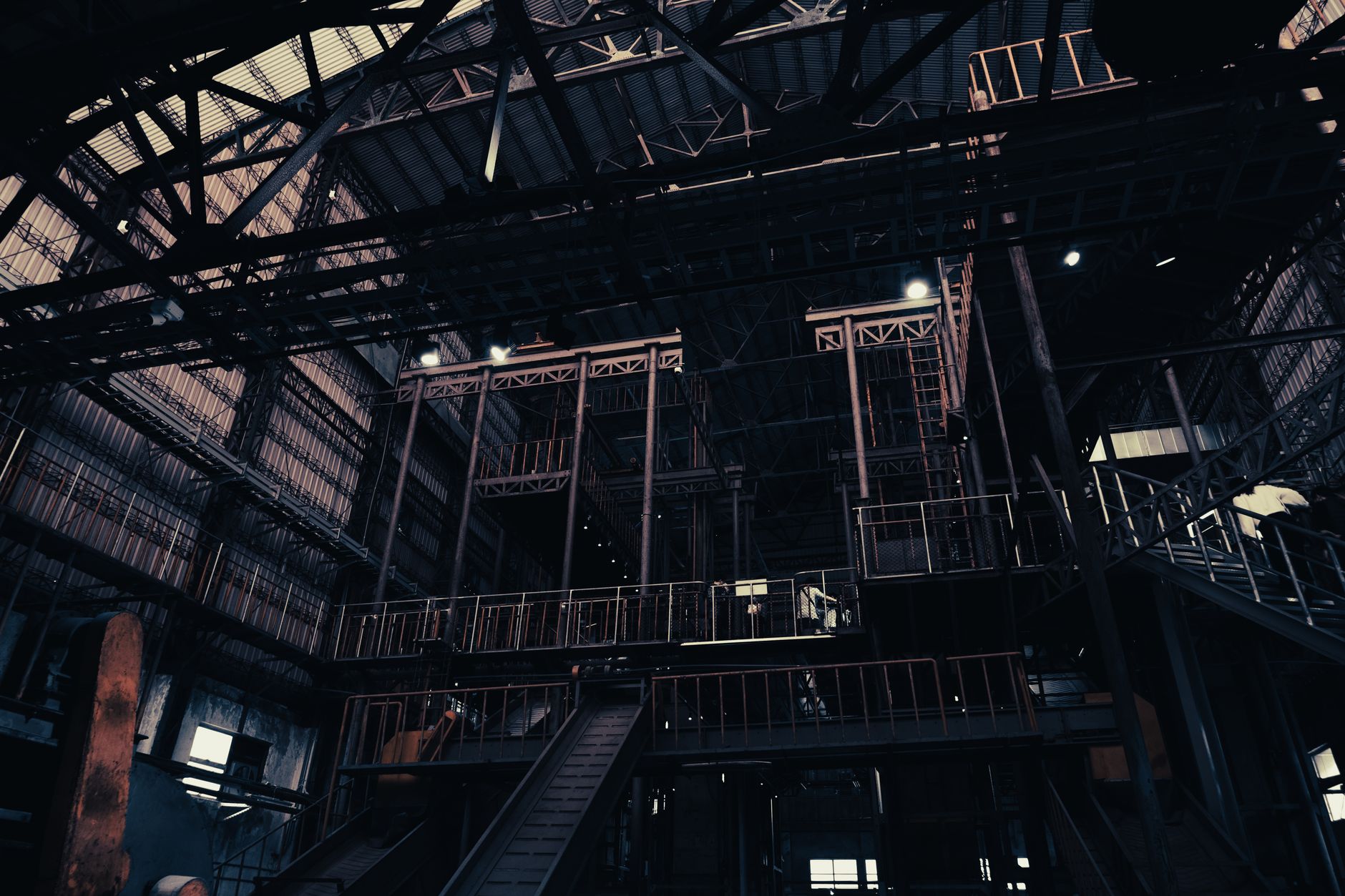 rows of bomb tail-kit assemblies staged on metal racks inside a large defense manufacturing warehouse, with overhead lighting illuminating the production floor