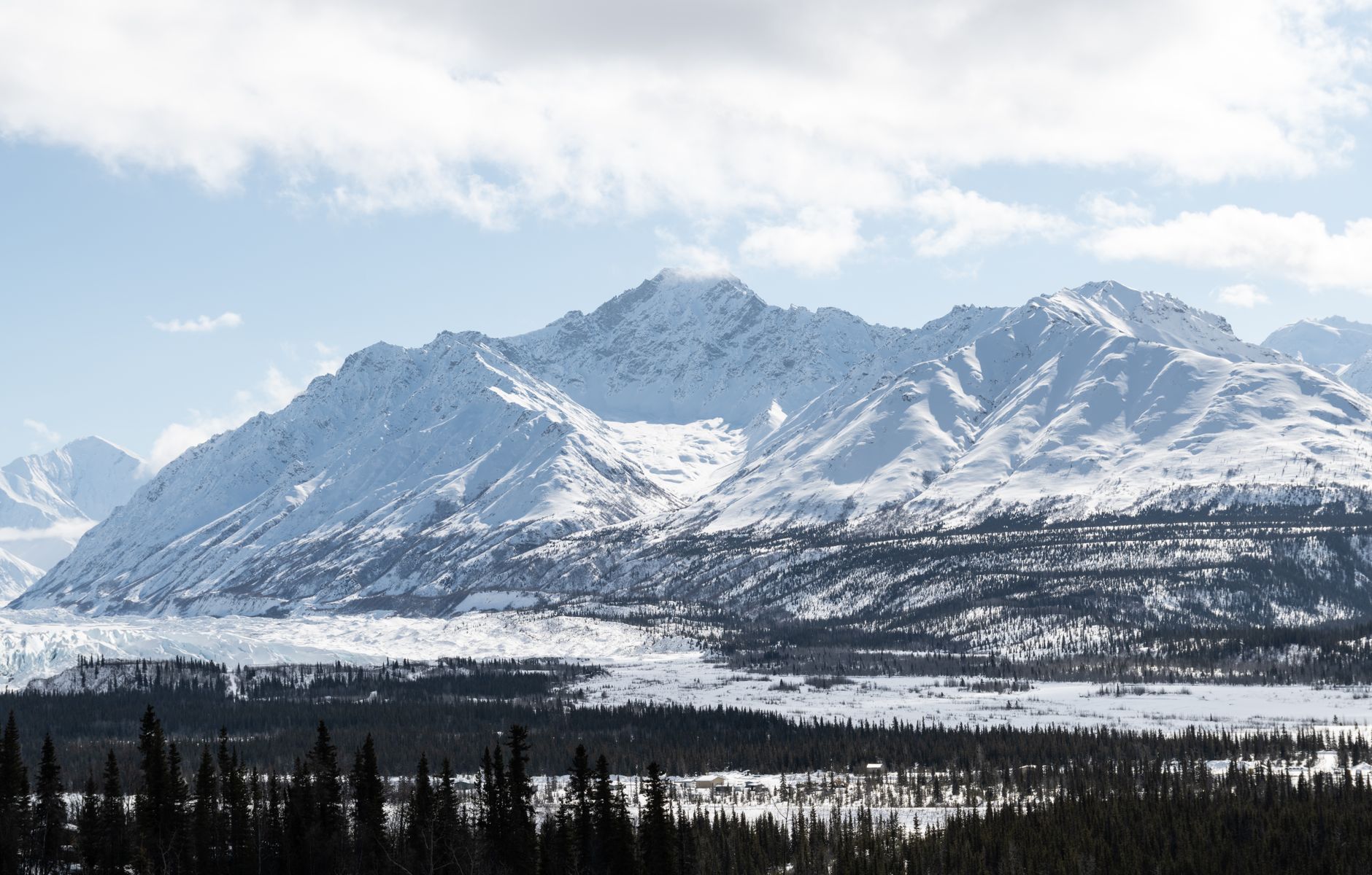 a remote U.S. military airfield in Alaska with snow-dusted tarmac, low prefabricated support structures, and mountain terrain visible in the background