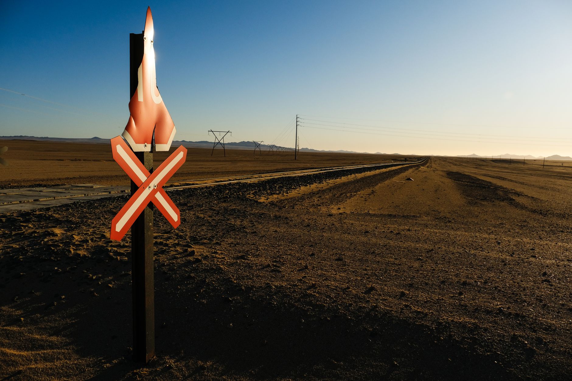 a vertical launch missile defense interceptor on its ground-based launch rail in an open desert test facility, wide environmental shot with support equipment visible in the background