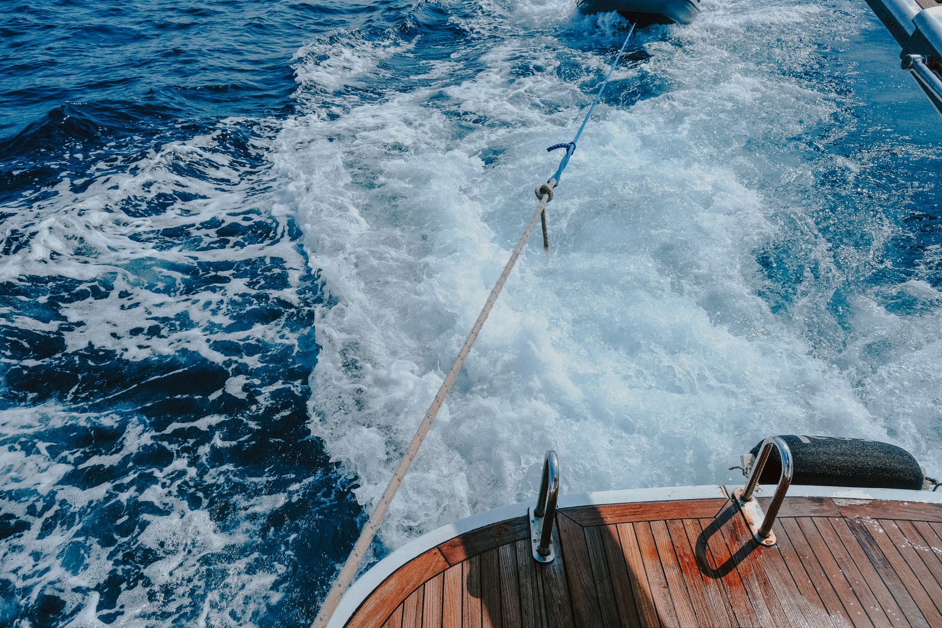 a compact unmanned surface vessel underway on open ocean, towing cable visible at stern, solar panels mounted on hull deck