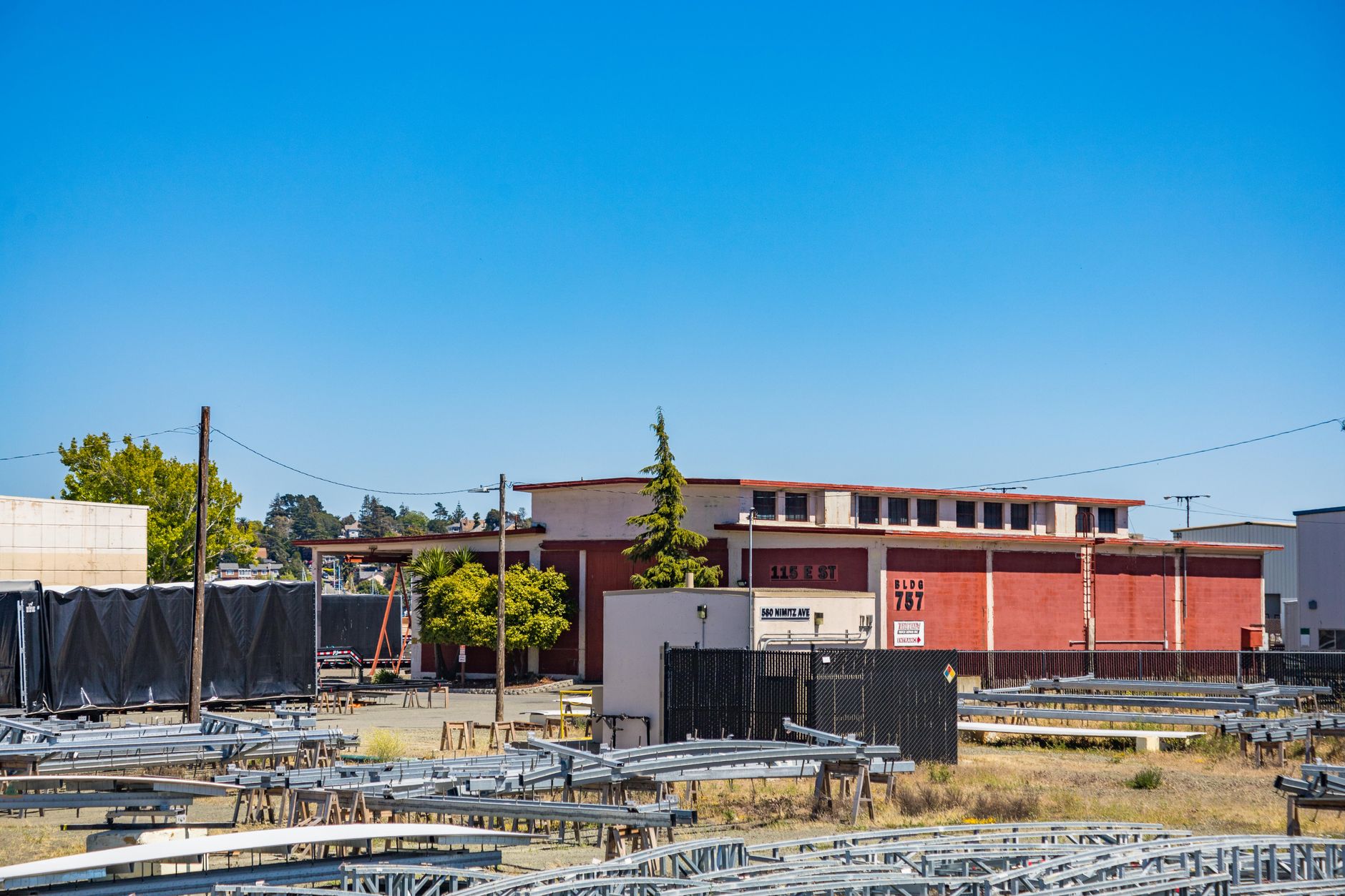 an aerial view of a large defense manufacturing complex with parking areas and warehouse structures, taken in daylight from a distance showing the full facility footprint