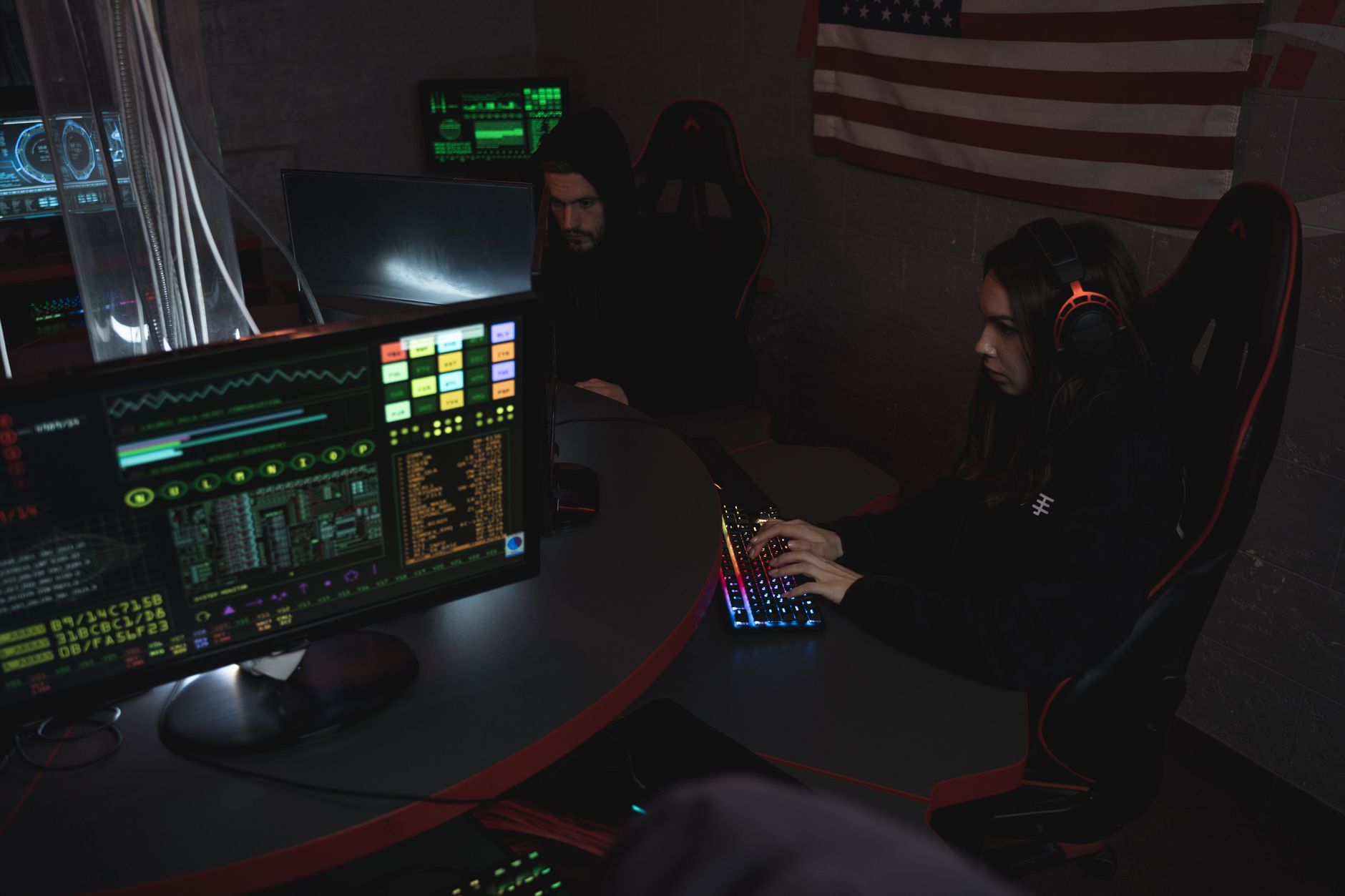 a large cybersecurity operations center with illuminated monitor arrays displaying global network threat maps, workstations in the foreground, low ambient lighting