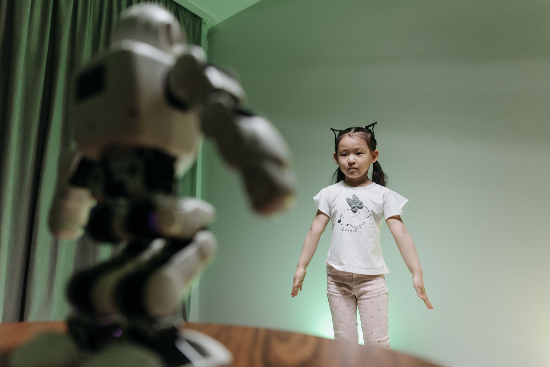 a bipedal humanoid robot mid-stride on an indoor track at a large robotics demonstration facility, with technical equipment and cameras visible along the sidelines