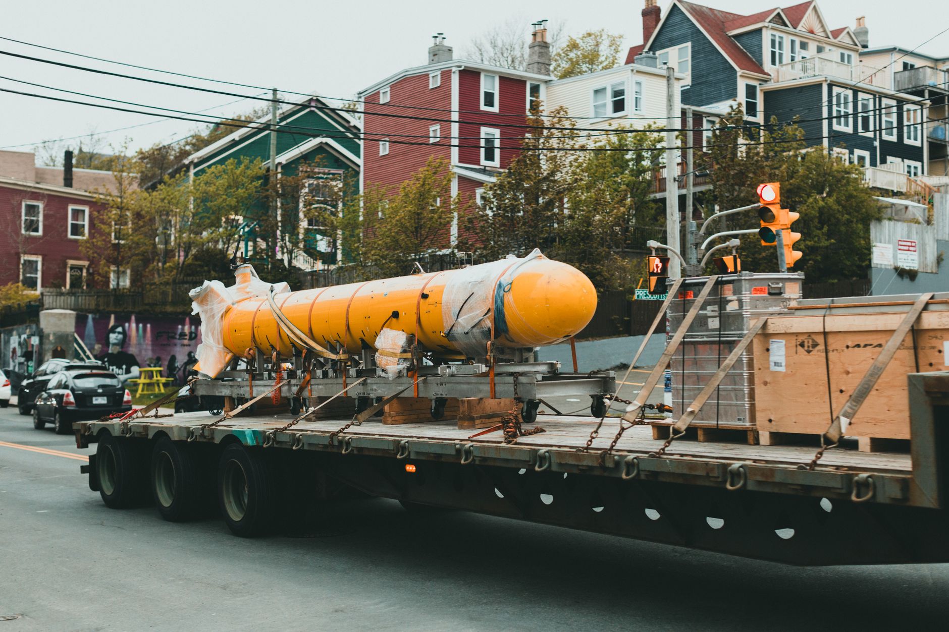 a horizontal rocket booster being transported on a wheeled carrier vehicle through an industrial processing facility, technicians in cleanroom gear visible along the walls