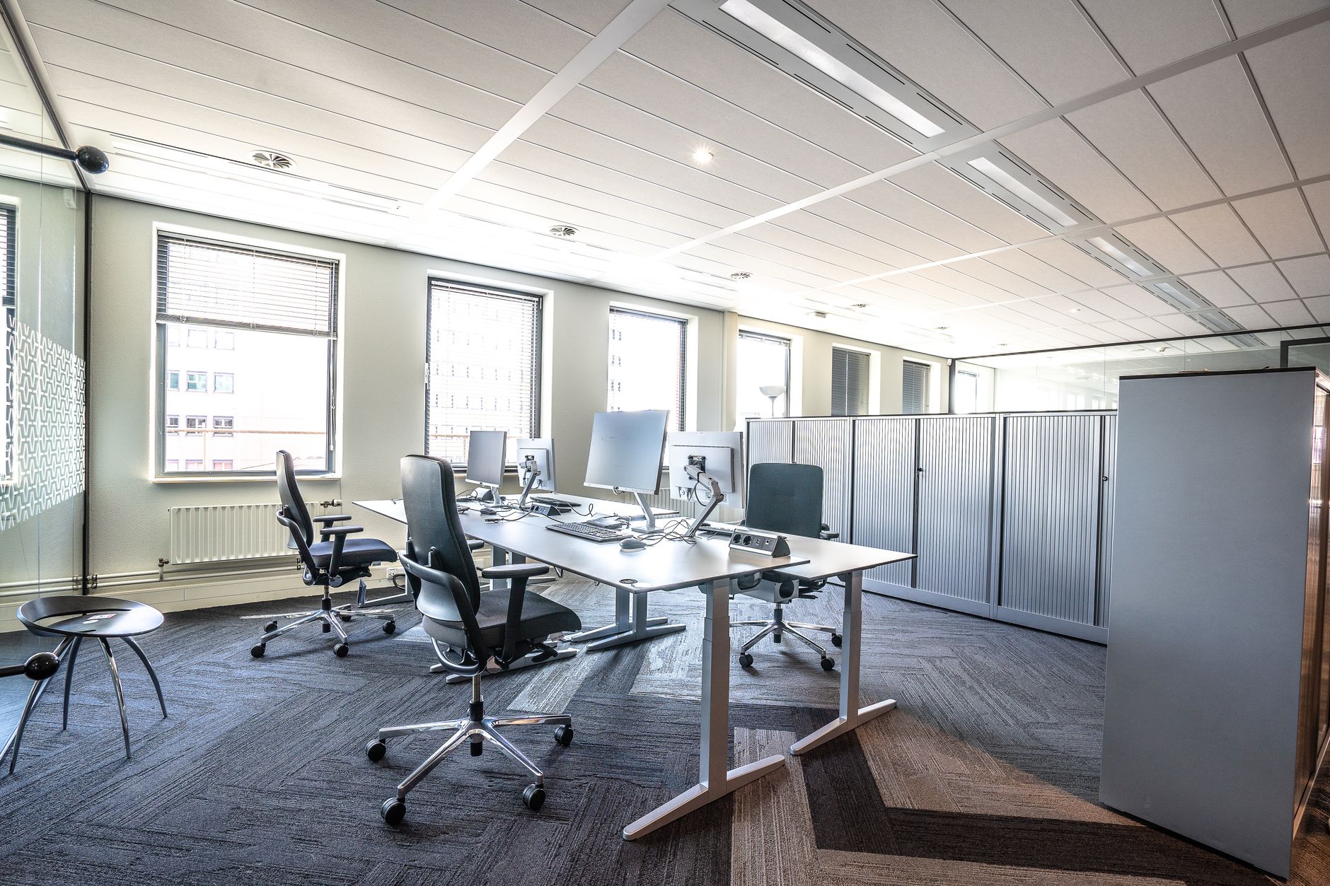an open-plan technology office interior with rows of workstations and servers visible through a glass partition, no people as focal point