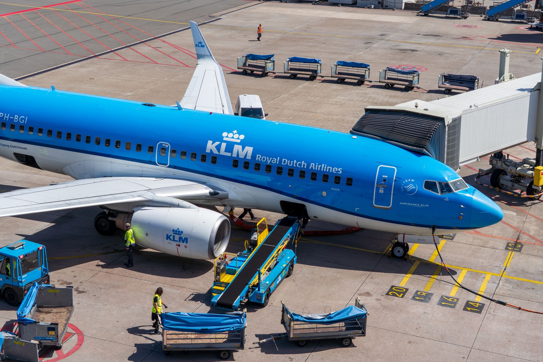 a wide-body commercial jet parked at a jetway on an airport apron, ground service equipment visible in the background, no markings close enough to read clearly