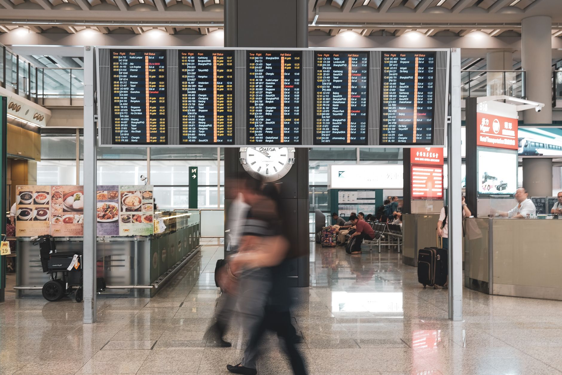 an international airport terminal interior with wide concourses, departure boards, and aircraft visible through floor-to-ceiling windows on the tarmac outside