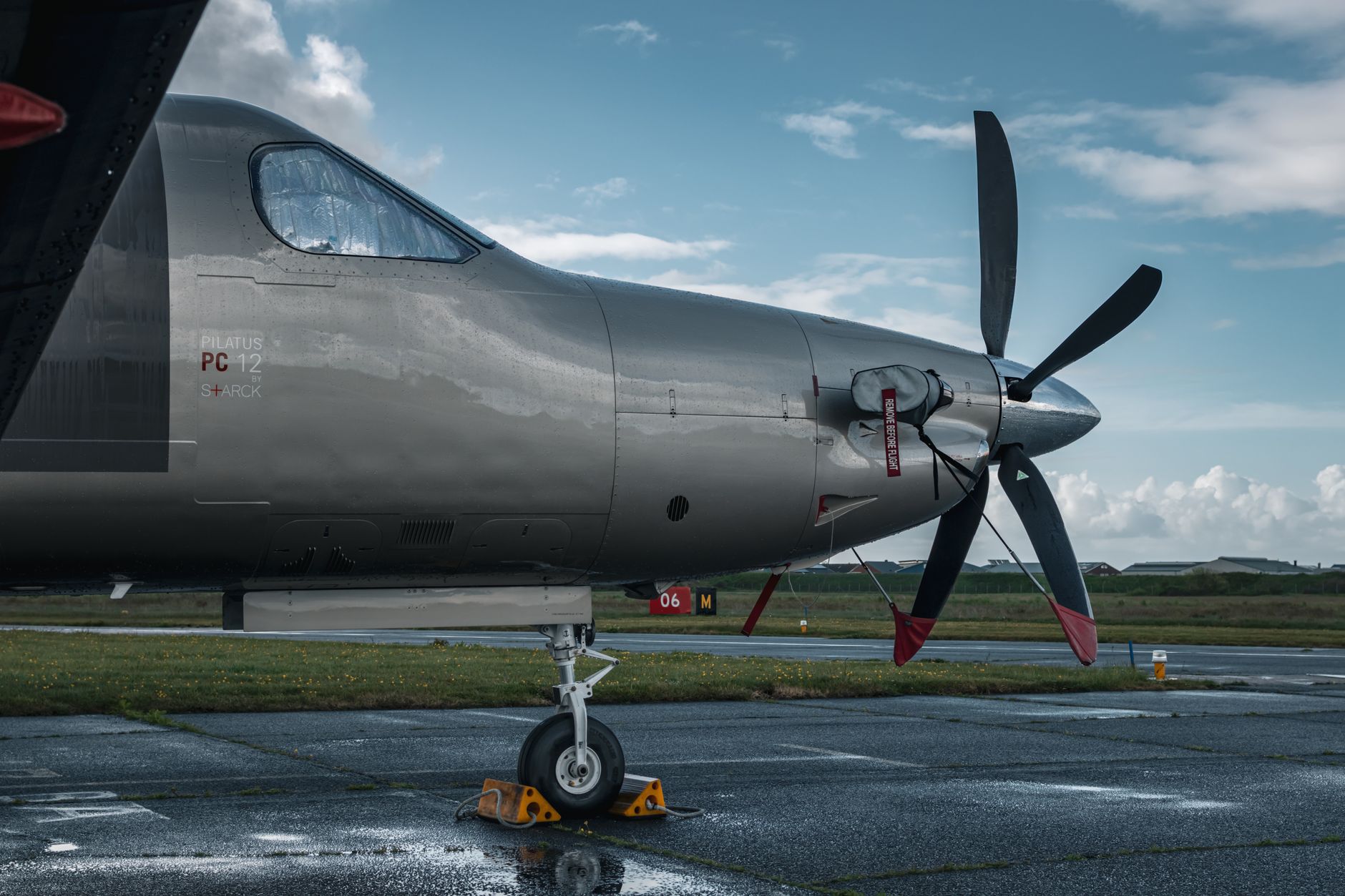 a turboprop military aircraft in a hardened aircraft shelter, with technicians in coveralls working around an external pod mounted beneath the fuselage