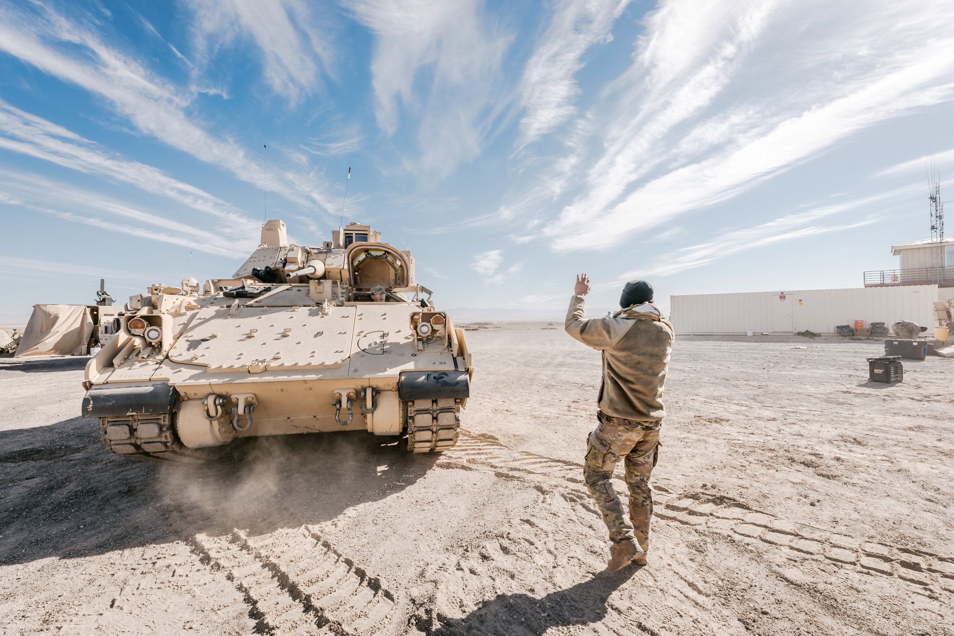 a high-powered laser test apparatus mounted on a ground-based military vehicle in an open desert testing range, with emitter housing visible and technicians' equipment in the background