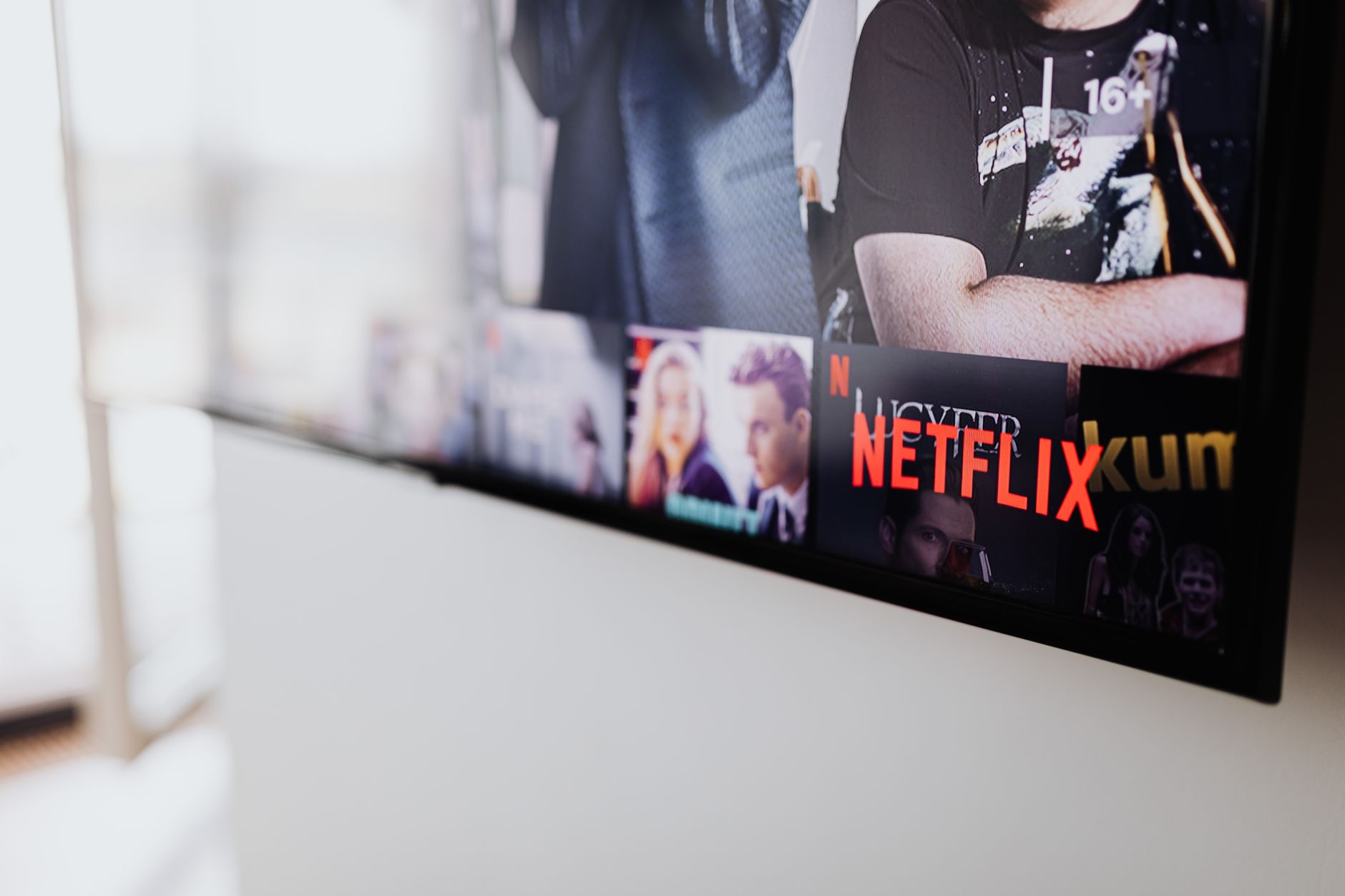 a streaming service interface displayed on a laptop screen showing a fantasy drama series thumbnail grid, device resting on a wooden desk