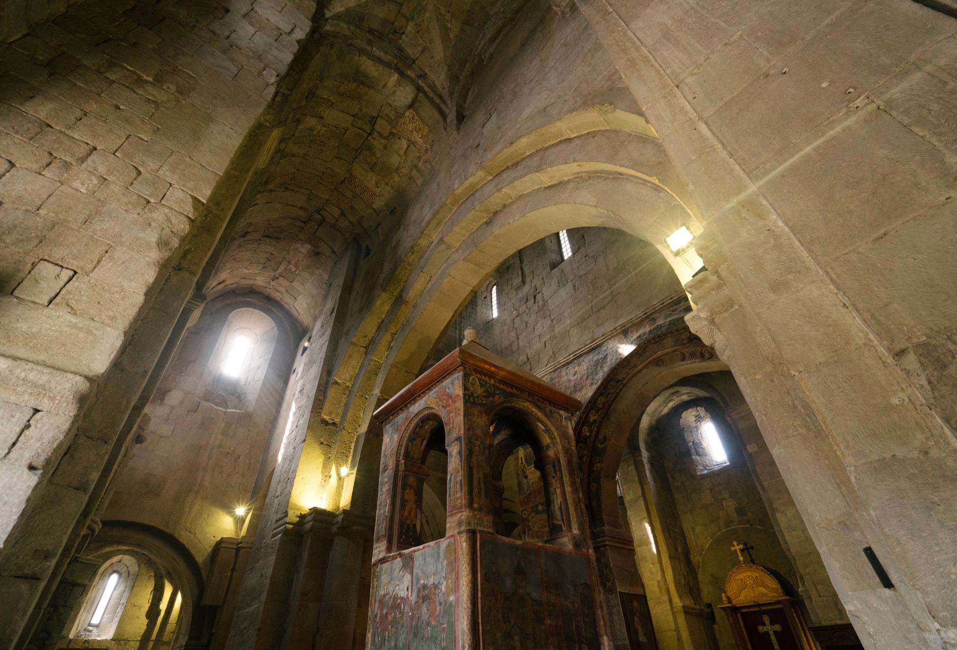 a grand medieval stone throne room with high vaulted ceilings, lit by torch sconces and a single shaft of natural light through a narrow window, empty of people