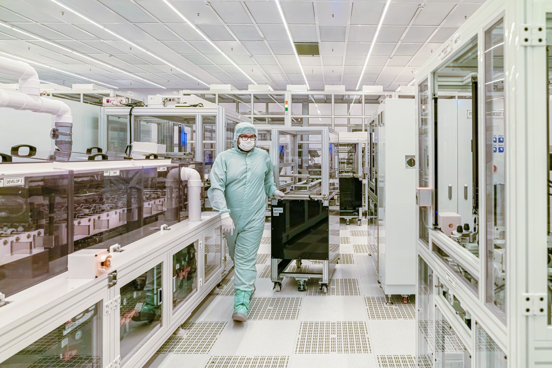 a large geostationary communications satellite in a cleanroom assembly facility, solar arrays partially extended, technicians in protective suits visible in the background