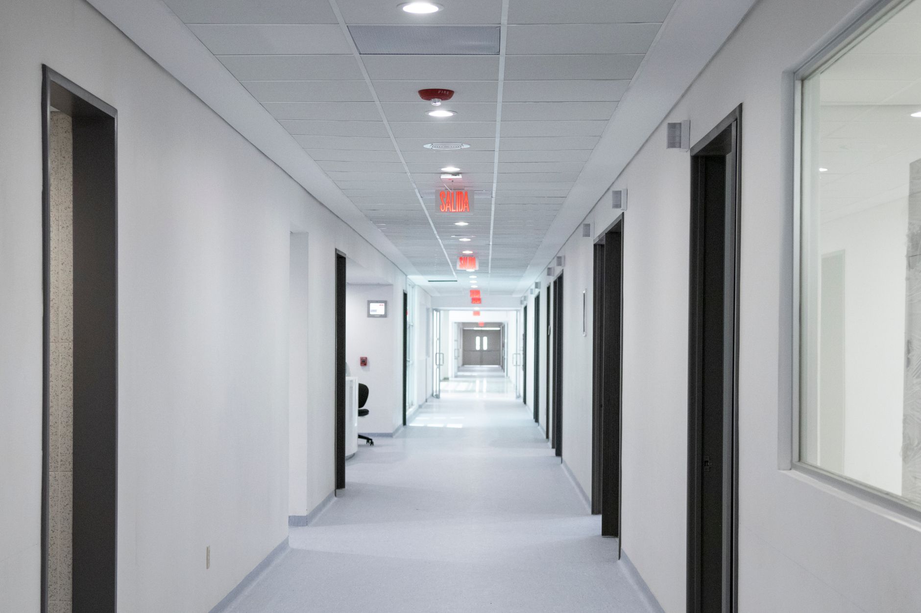 an empty hospital corridor with soft overhead lighting, medical equipment visible along the walls, a wheelchair parked near a doorway