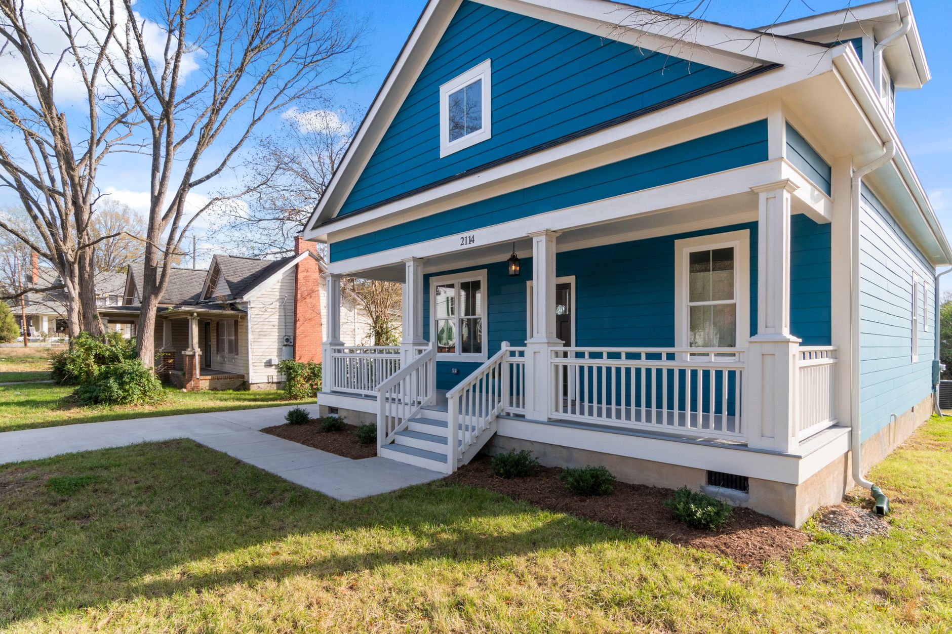 a quiet residential street in a small midwestern town, modest single-family homes with front porches, mature trees lining the sidewalk, no people as focal point