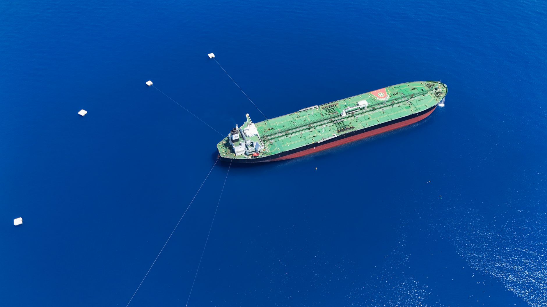 aerial view of a large oil tanker anchored in open water near a coastal terminal, no identifying markings visible