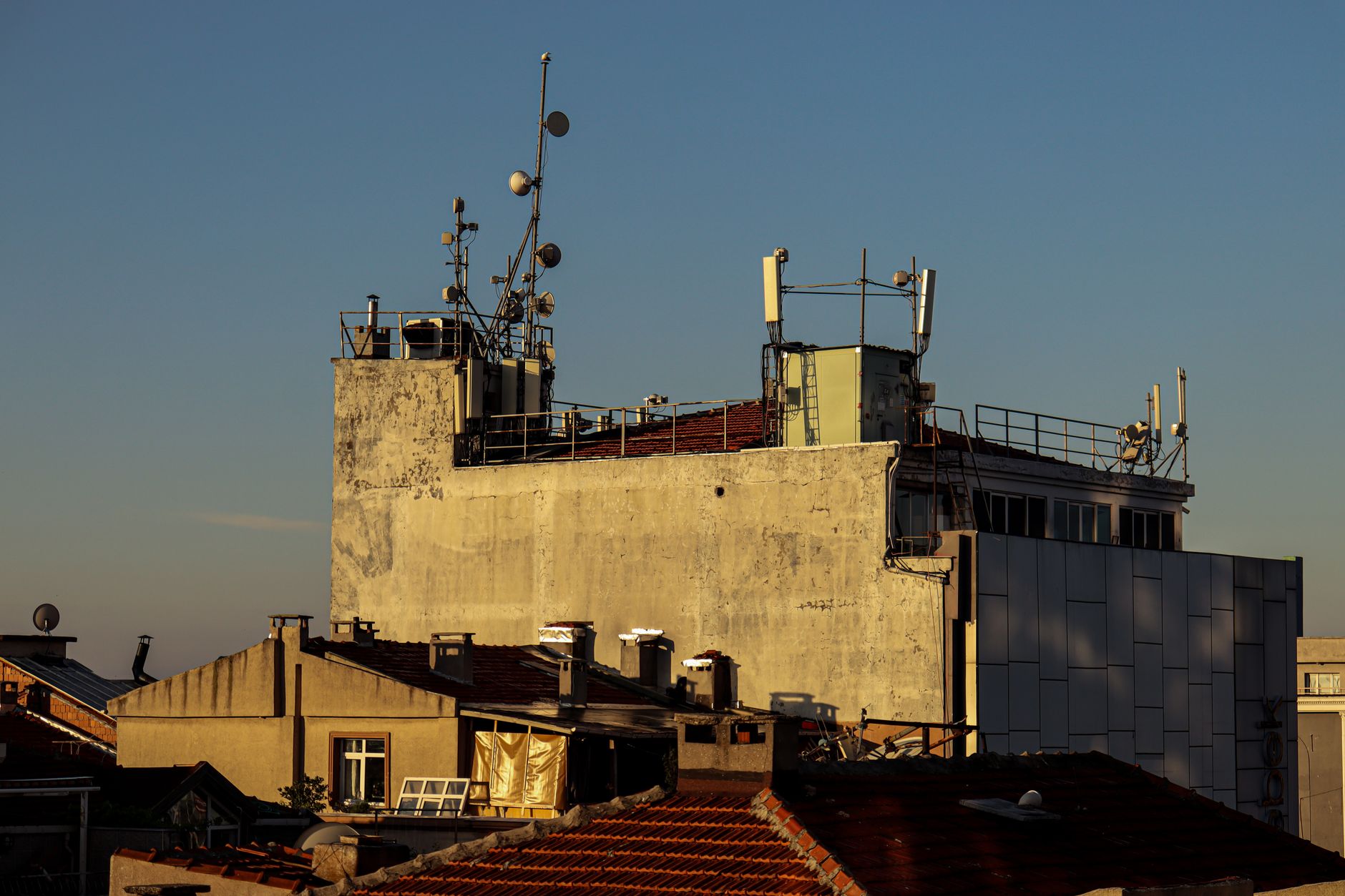 a military base perimeter fence viewed from outside, with communications towers and satellite dishes visible in the background against an open sky