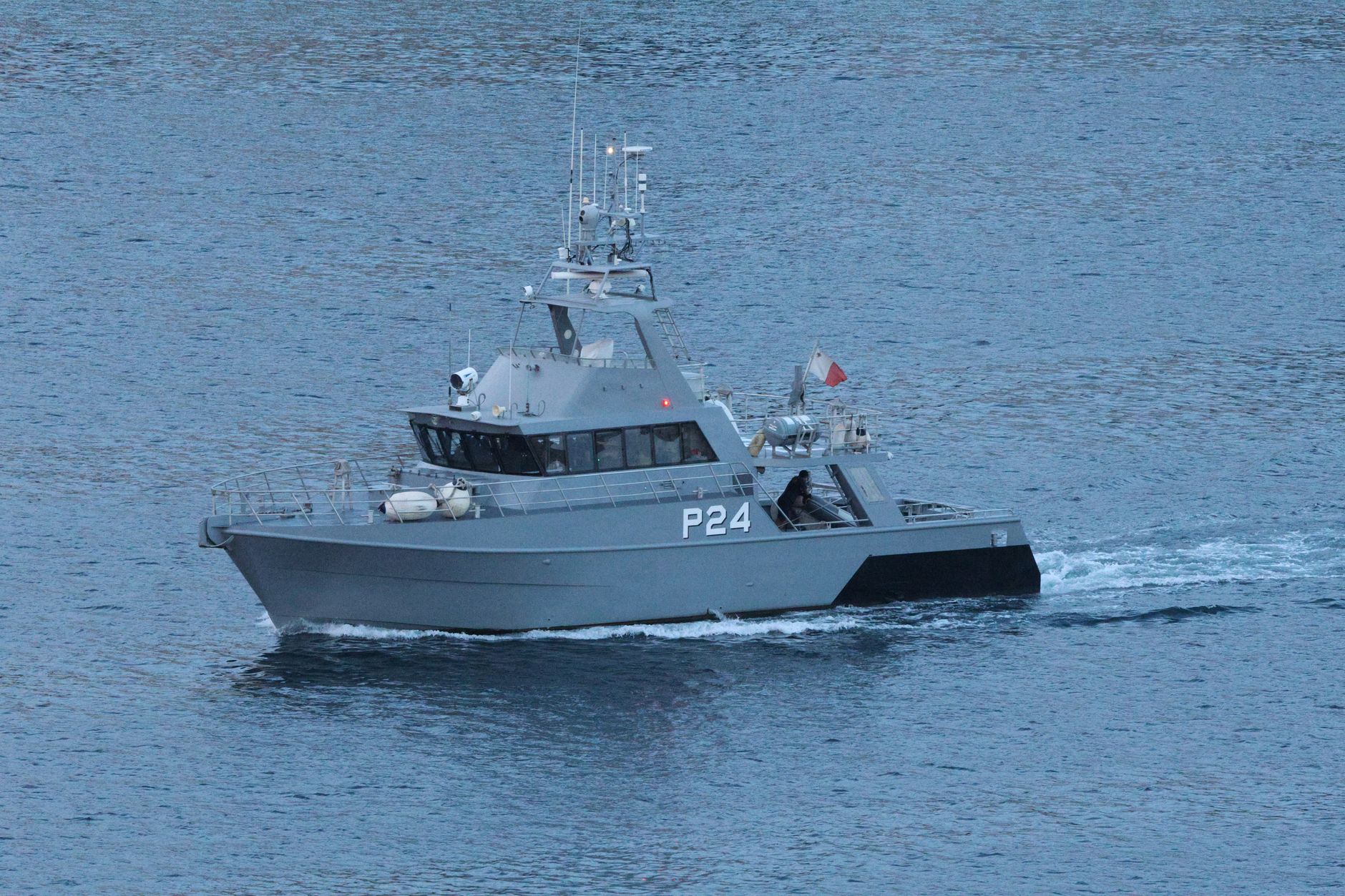 a gray IRGC fast-attack patrol vessel moored at a Persian Gulf naval dock, with desert shoreline and port infrastructure visible in the background