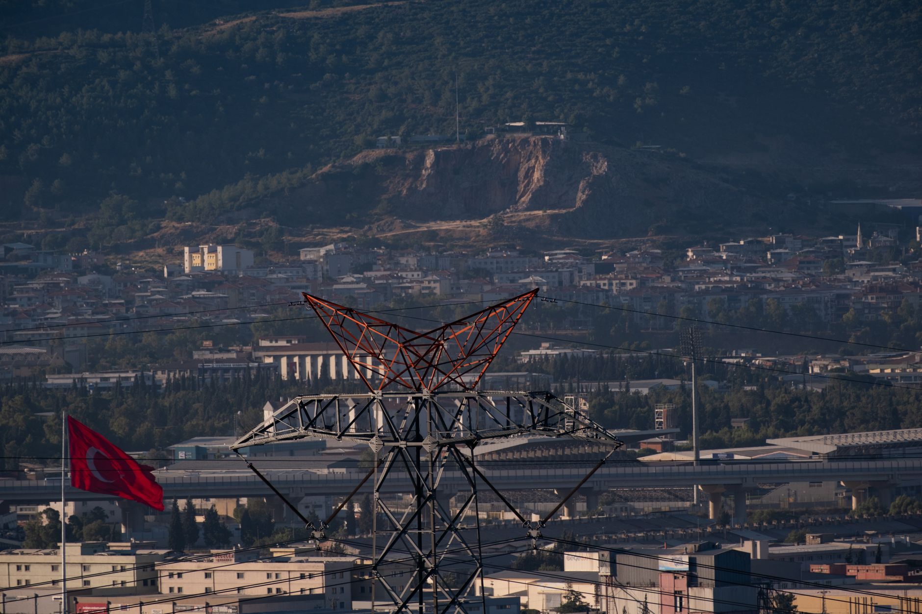 aerial view of a large government ministry building with Israeli flags, surrounded by urban infrastructure, midday lighting
