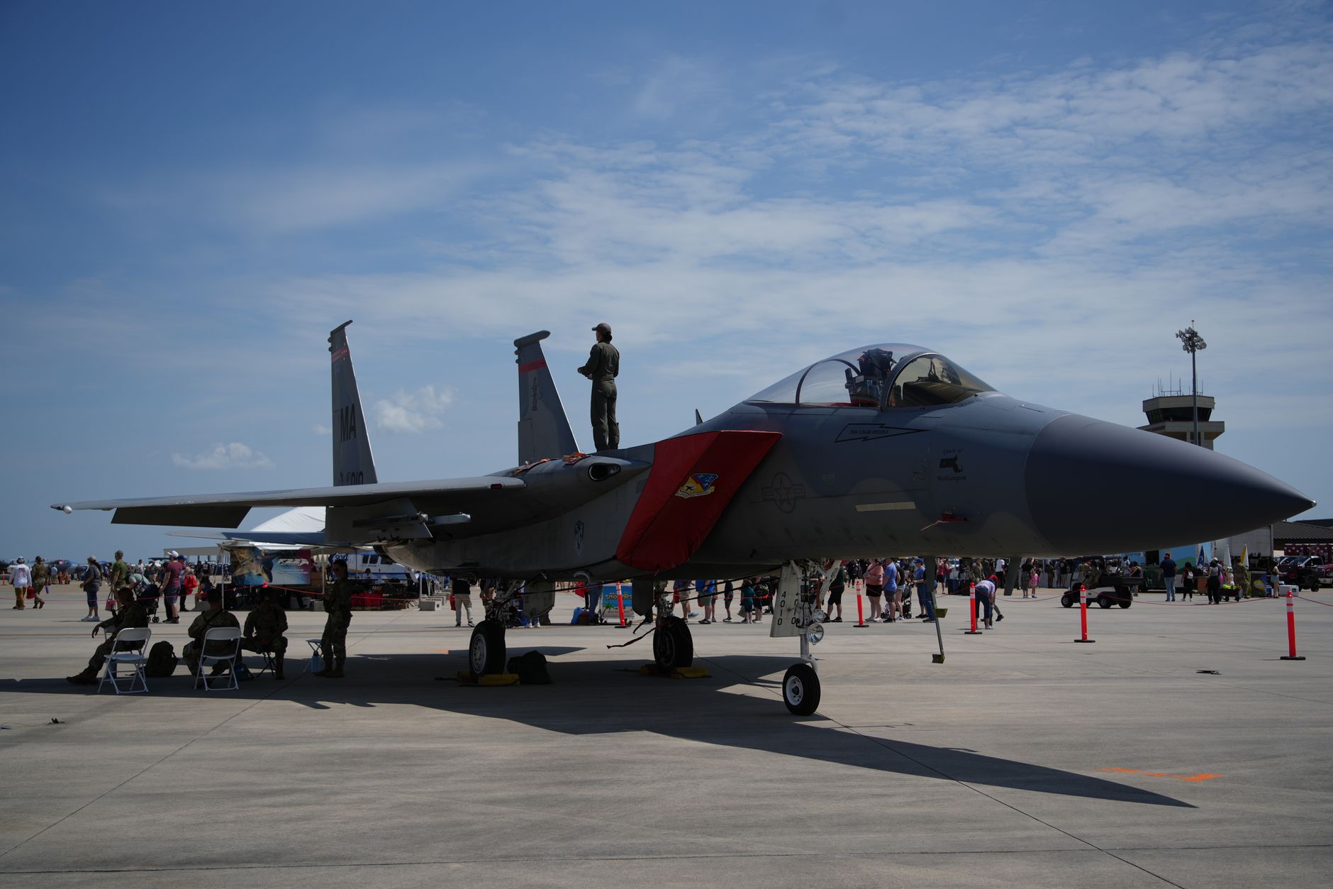 rows of F-15 aircraft parked on a sun-lit military flight line, maintenance equipment positioned near the nearest aircraft's engine bays, no personnel as focal point