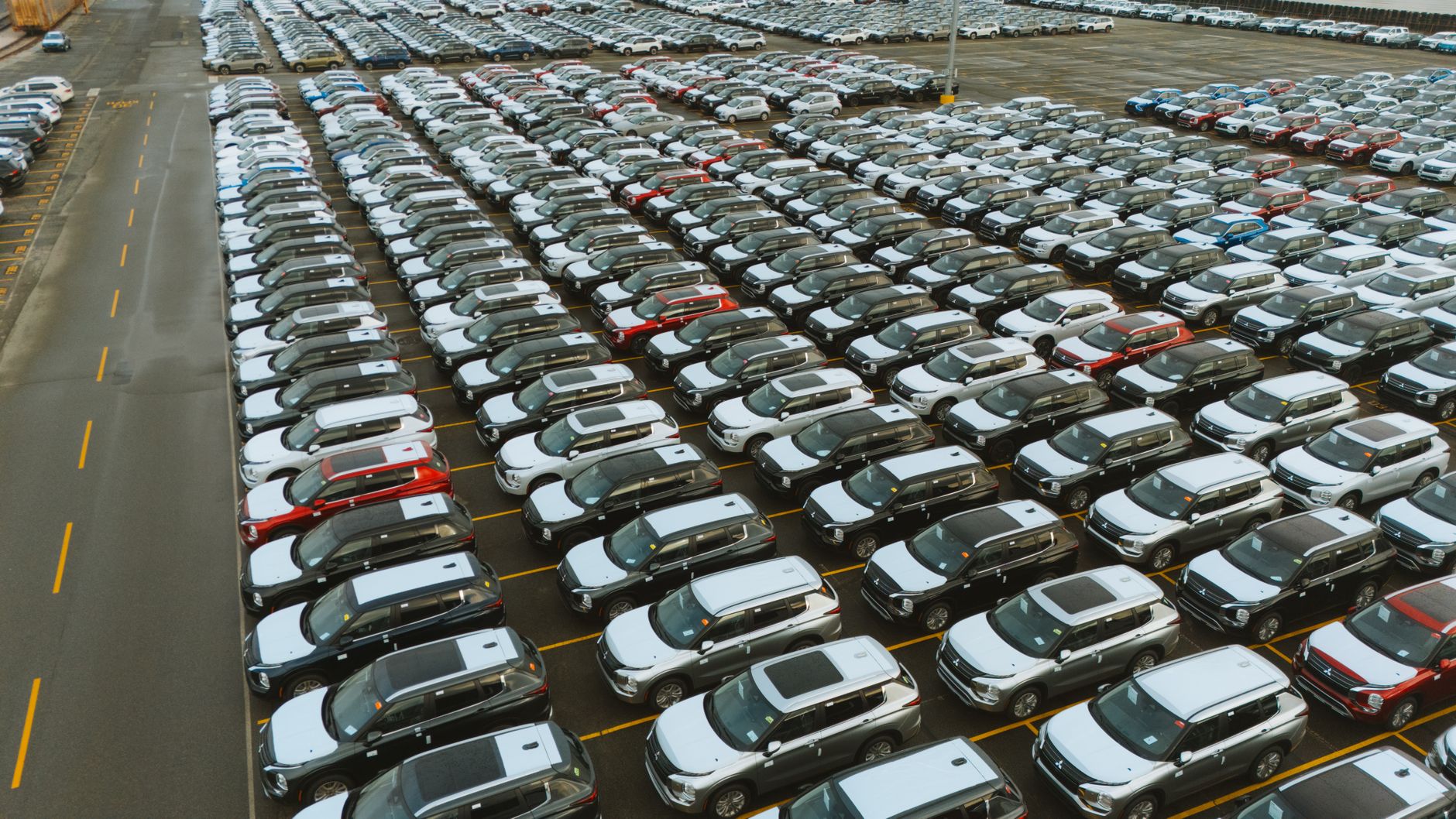 rows of armored personnel carriers staged at a large military logistics depot, overhead wide-angle view showing scale of equipment inventory