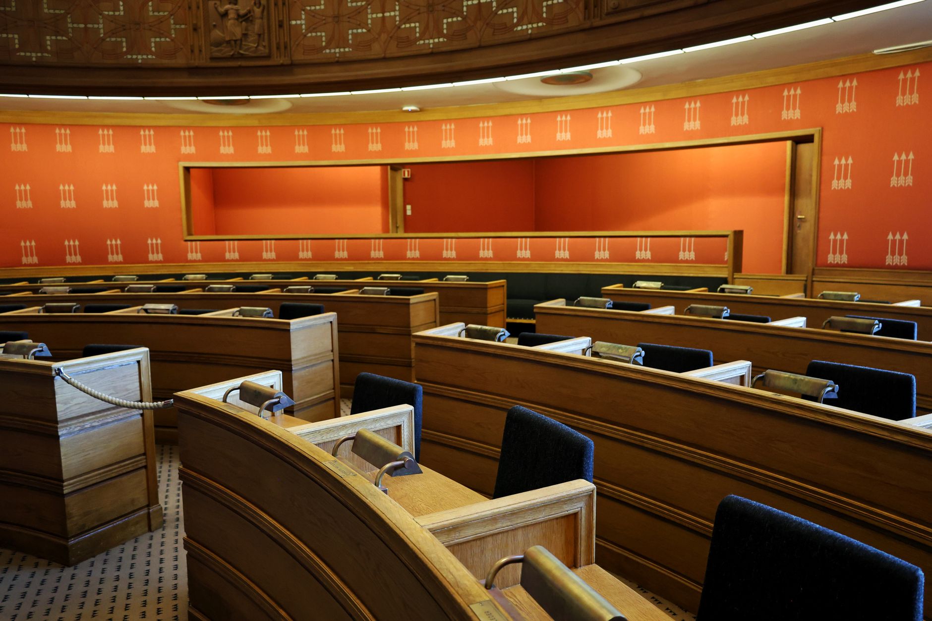 interior of a large government budget hearing room, wide-angle view showing officials seated at a long table with documents and screens, no faces identifiable