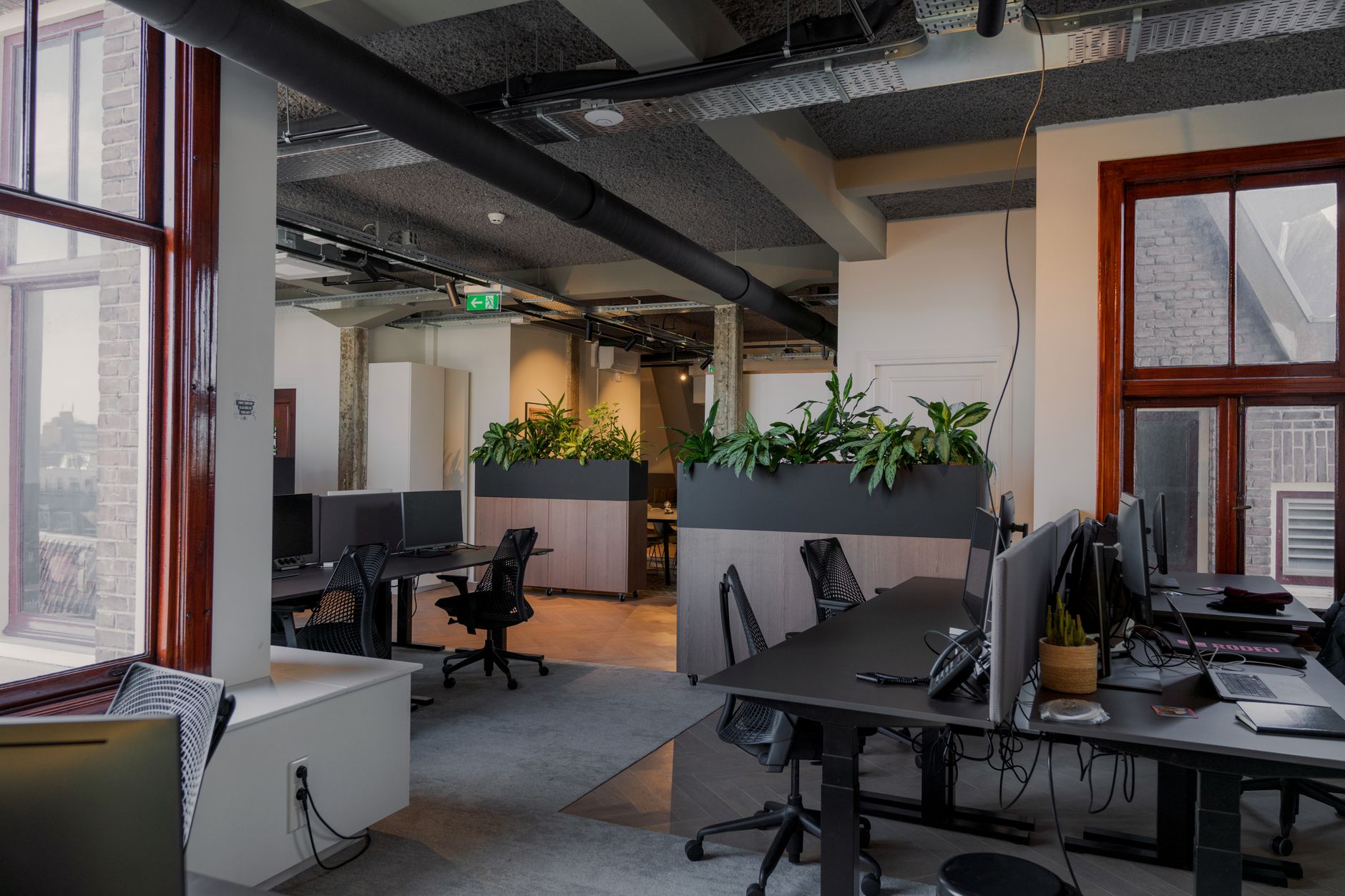 a modern open-plan technology office interior in Tel Aviv with rows of workstations, large monitors displaying data dashboards, and floor-to-ceiling windows overlooking an urban skyline