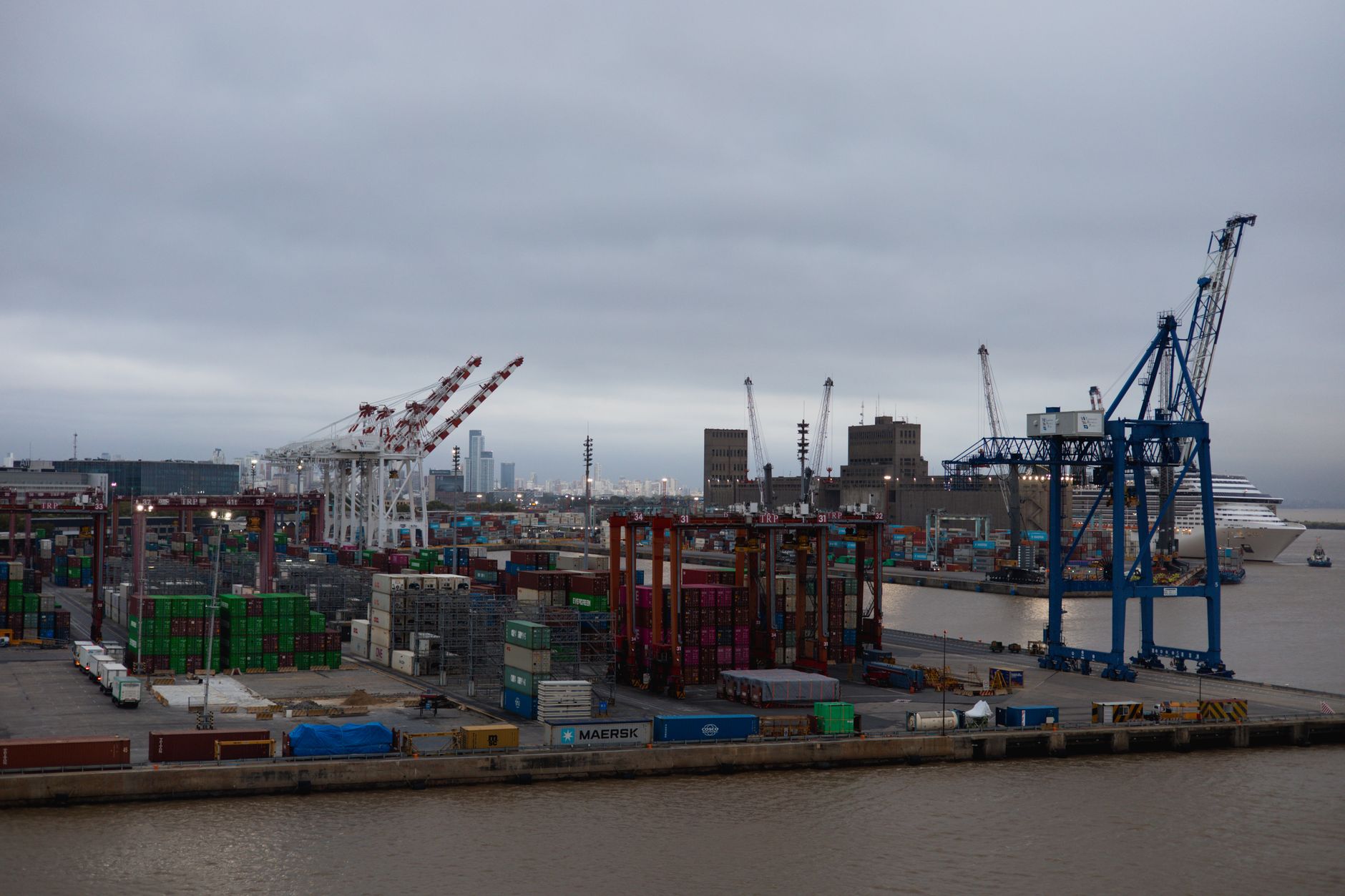 a wide-angle view of a Gulf Coast industrial waterfront with refineries and shipping infrastructure in the background under overcast skies, no people in foreground