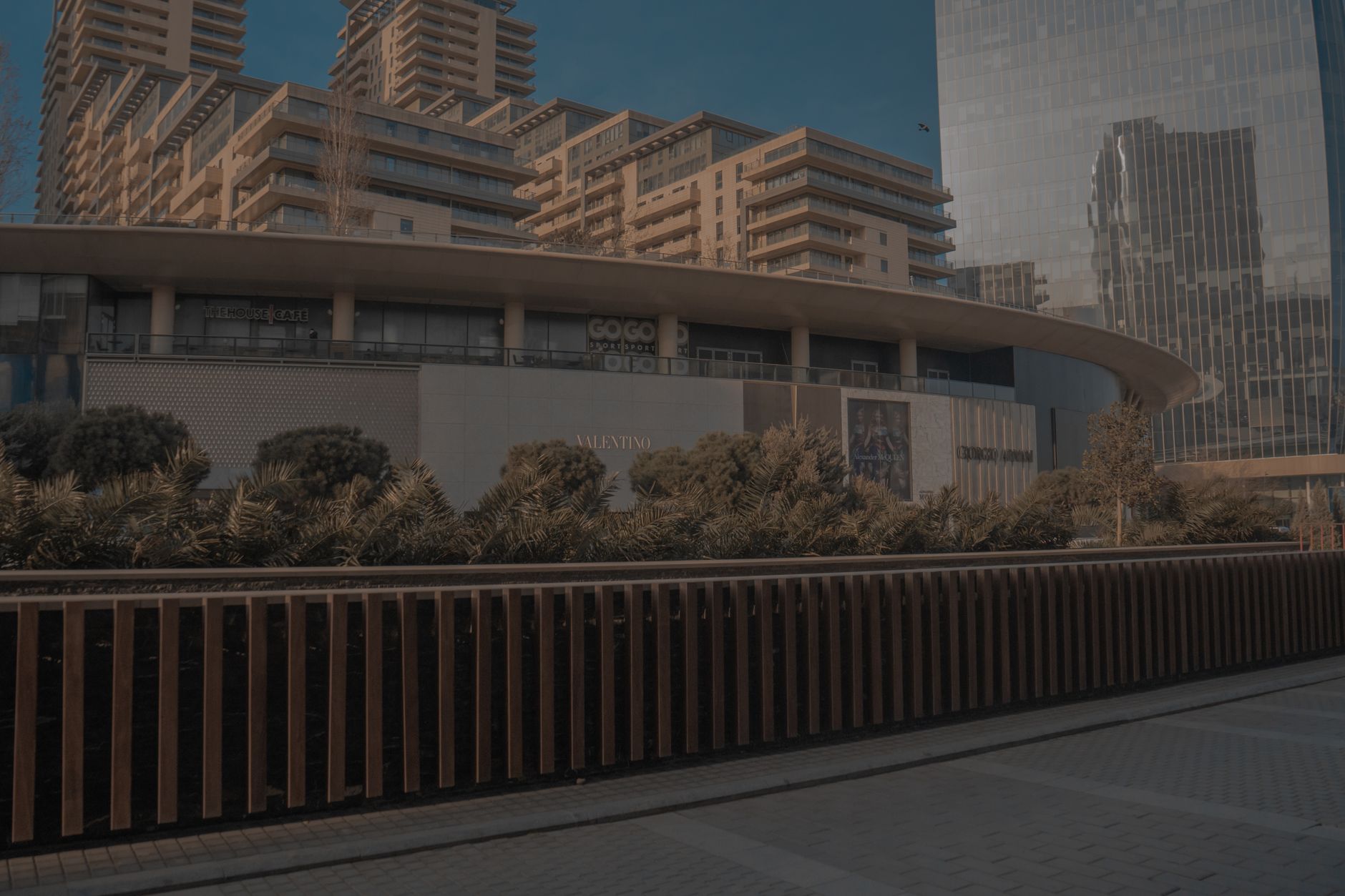 a small commercial drone on a concrete surface in an outdoor setting, urban buildings visible in the background, no people in foreground