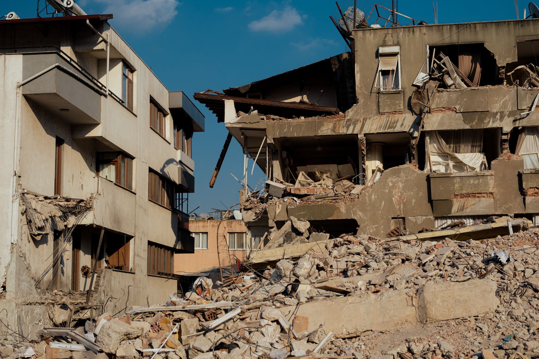 a partially destroyed residential apartment block in a Ukrainian city, debris scattered across a cracked pavement, no people visible in the foreground
