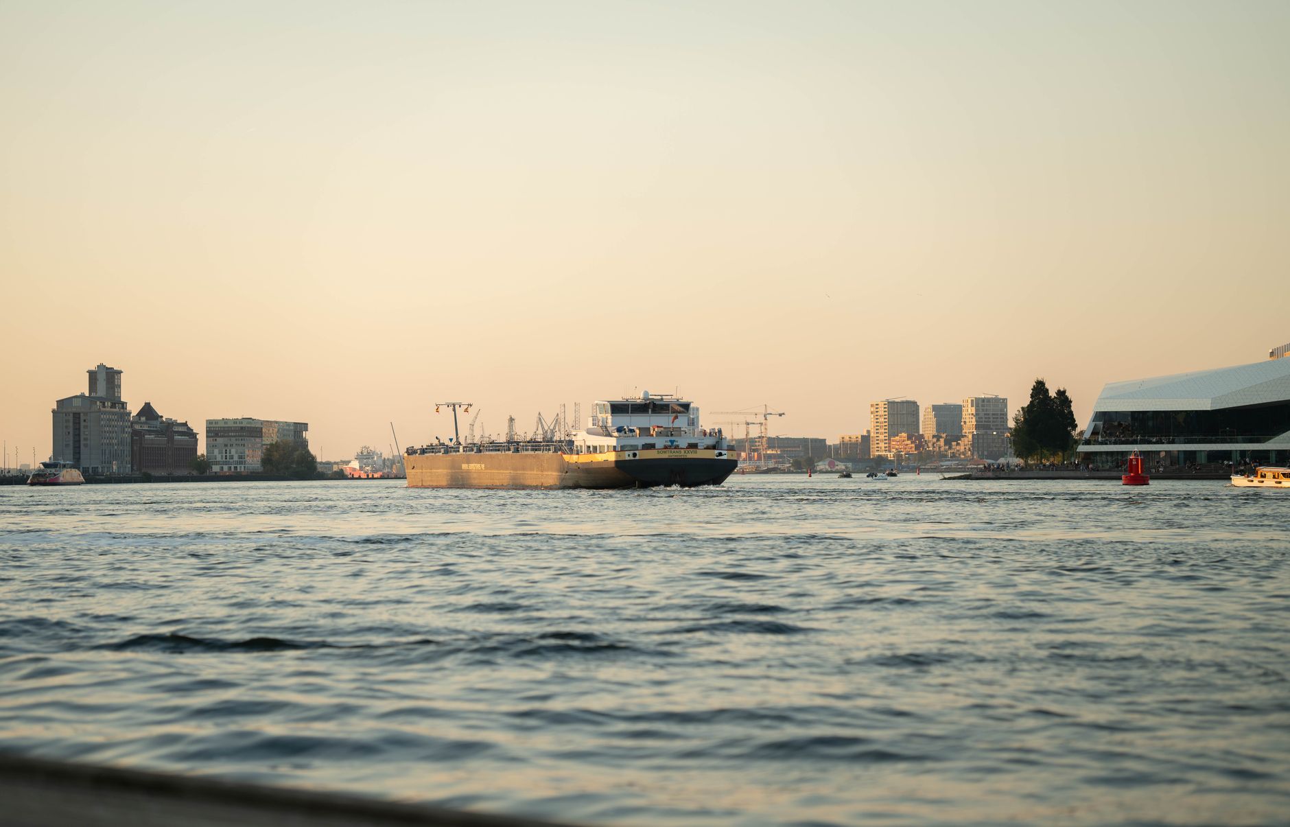 a wide-angle view of a river city skyline from across a large waterway, late afternoon light, buildings visible in the middle distance with no people foregrounded