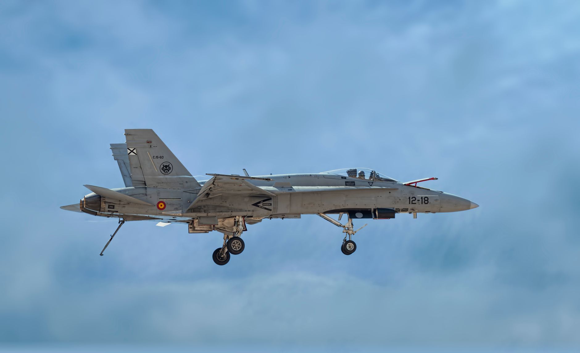 an F/A-18 Hornet parked on a flight line at a forward operating base, maintenance equipment staged around the aircraft, desert terrain visible in the background