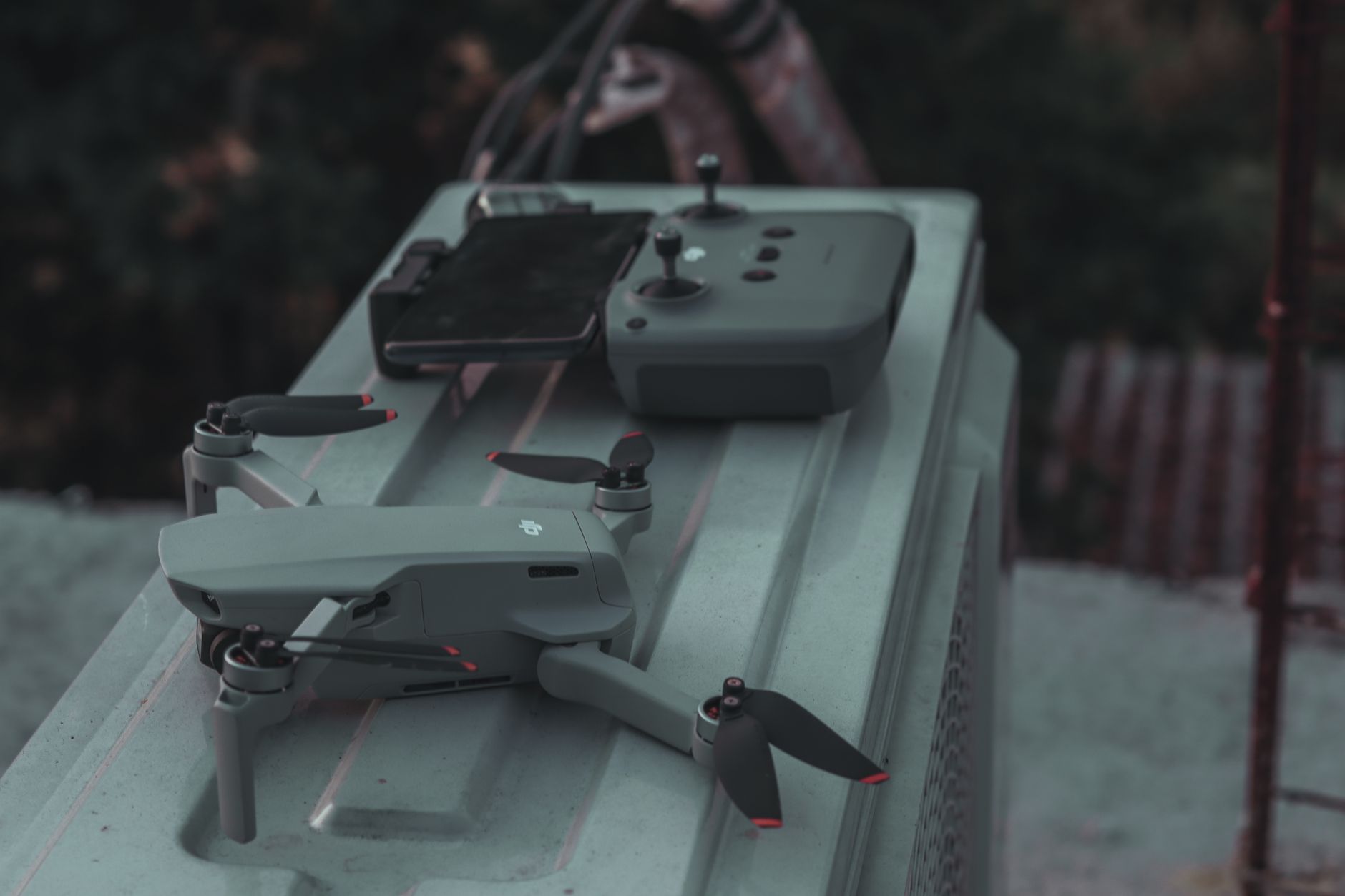 a close-up of a compact cylindrical drone launch tube resting on a field table at an outdoor military exercise site, with antenna equipment and a control unit visible nearby, no personnel in frame