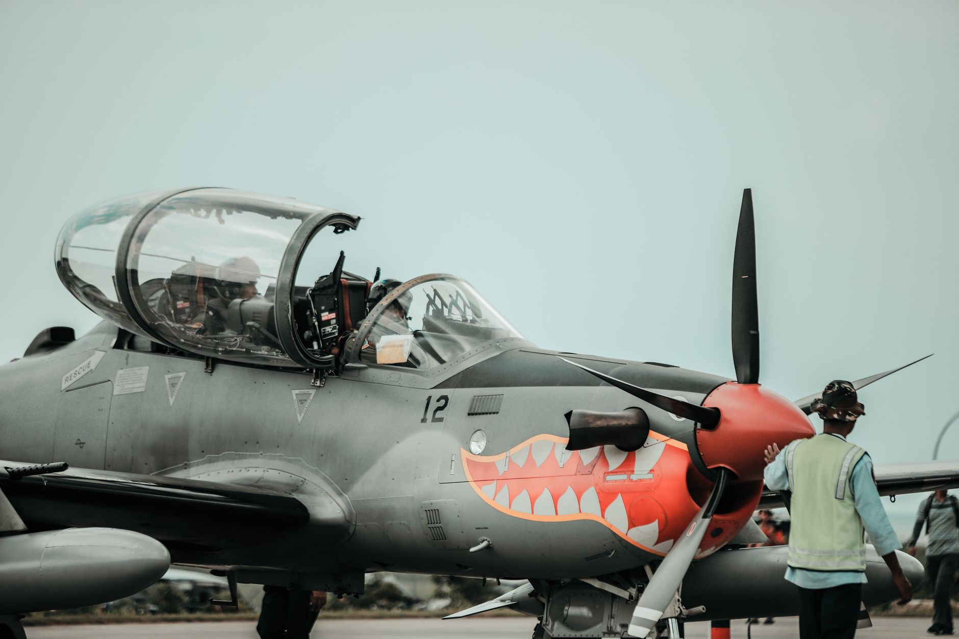 a carrier-based fighter aircraft on a flight deck with ground crew conducting a pre-flight inspection, ocean visible in the background