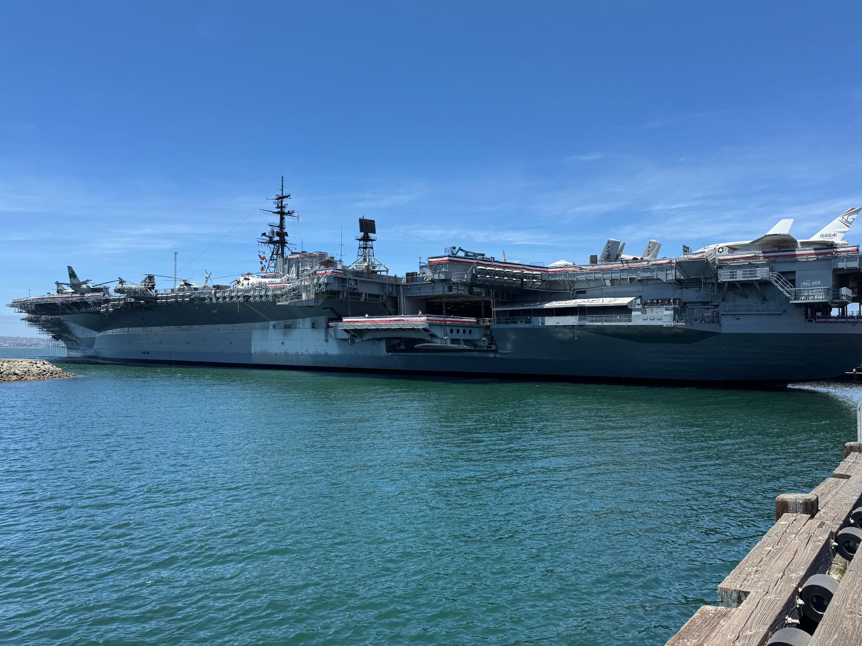 a carrier strike group's air wing aircraft parked in organized rows on a flight deck, with the island superstructure visible in the background at sea