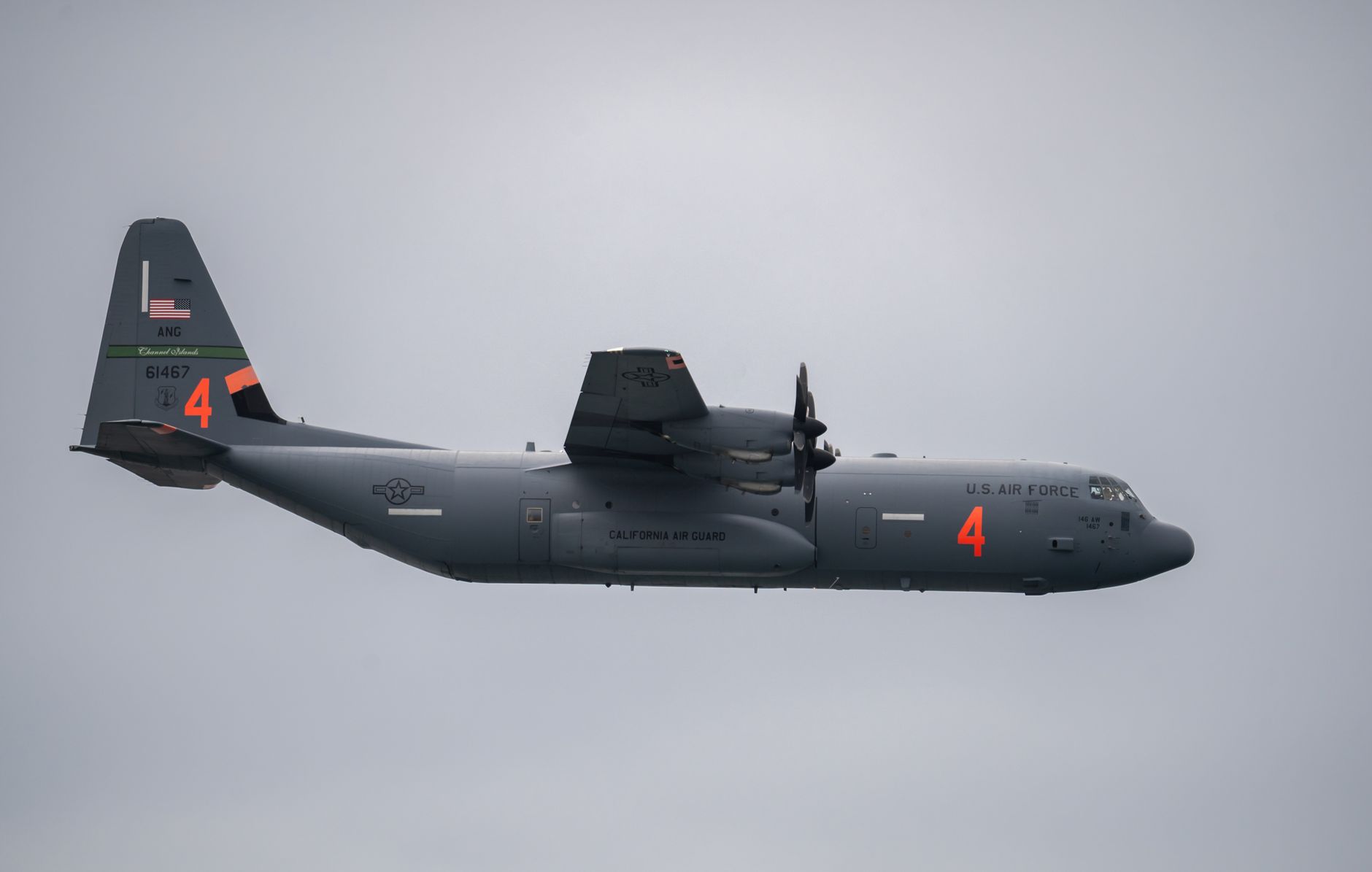 A C-130J Super Hercules aircraft parked on a flight line at a military air base, ground equipment and fuel trucks visible nearby