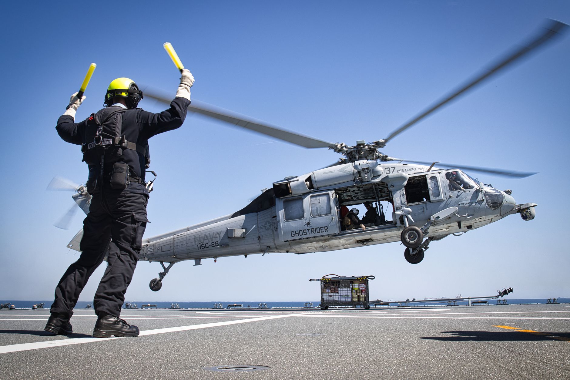 An E-2D Advanced Hawkeye aircraft parked on a carrier flight deck, rotodome visible above the fuselage, deck crew in the background
